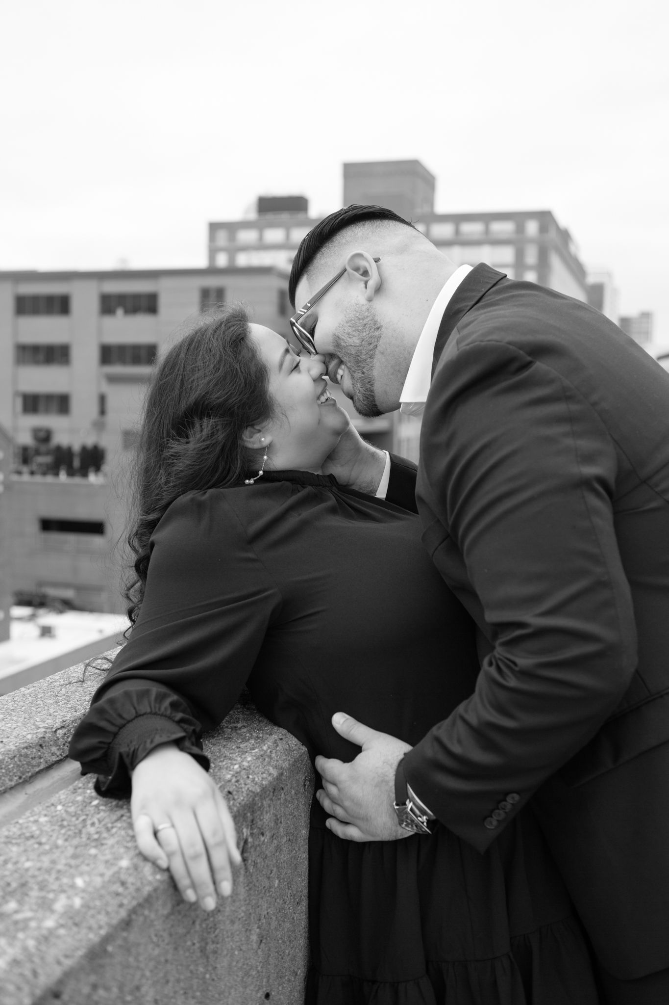 Elegant engaged couple smiling and embracing in downtown Louisville, with the woman showing her engagement ring