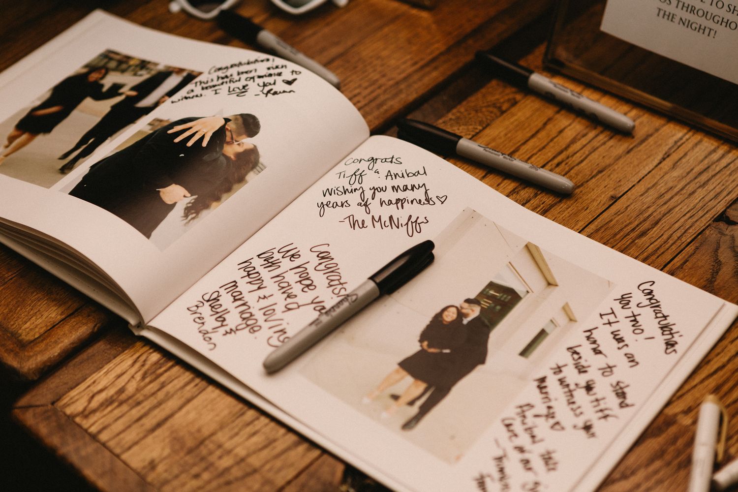 A guestbook or photo album lies open on a wooden table with handwritten notes and black and white photographs inside.