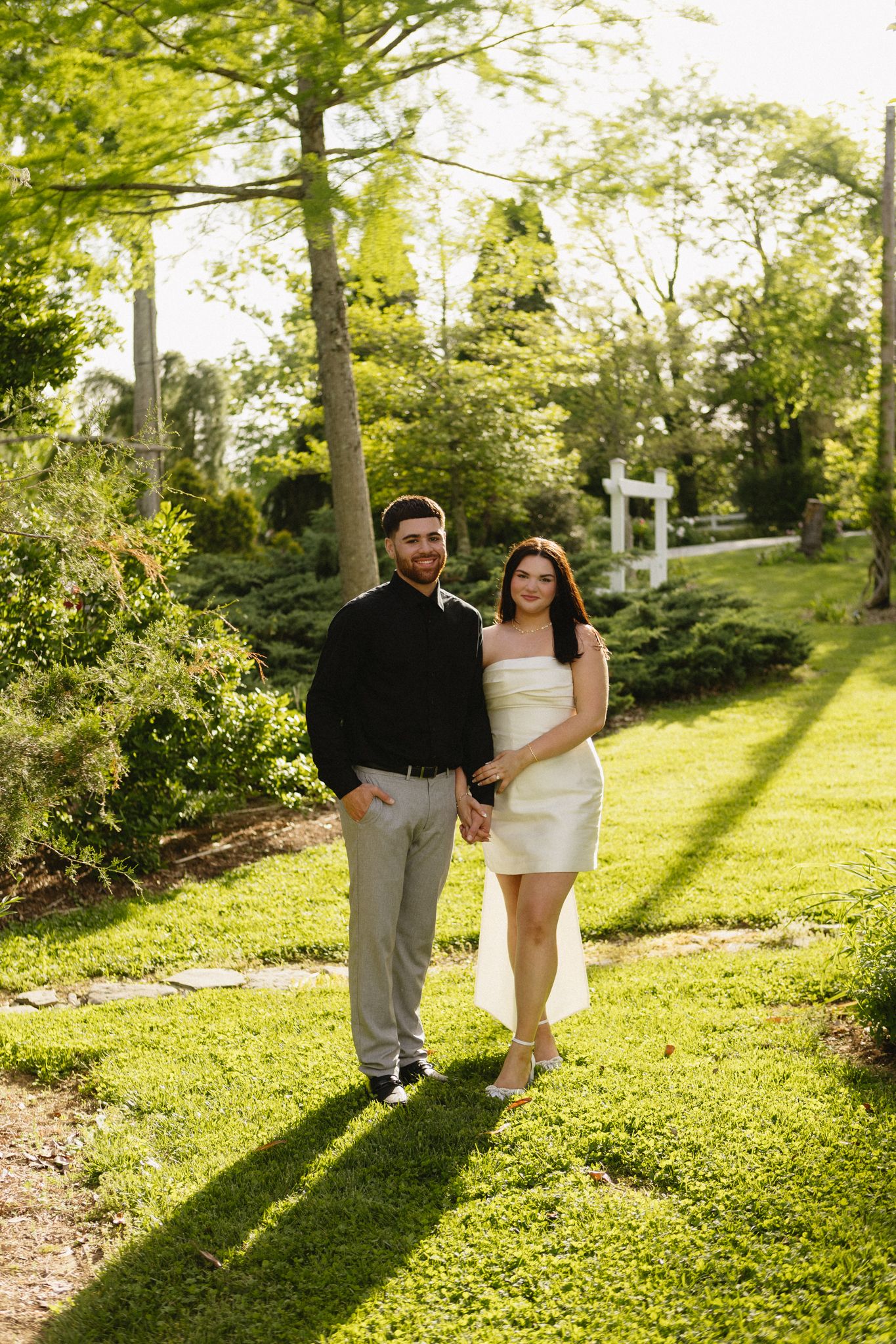 A couple walking through a sun-dappled garden pathway on a bright summer day.