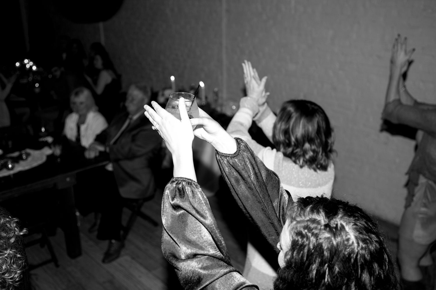 Black and white photo of wedding guests dancing with hands raised at reception party.