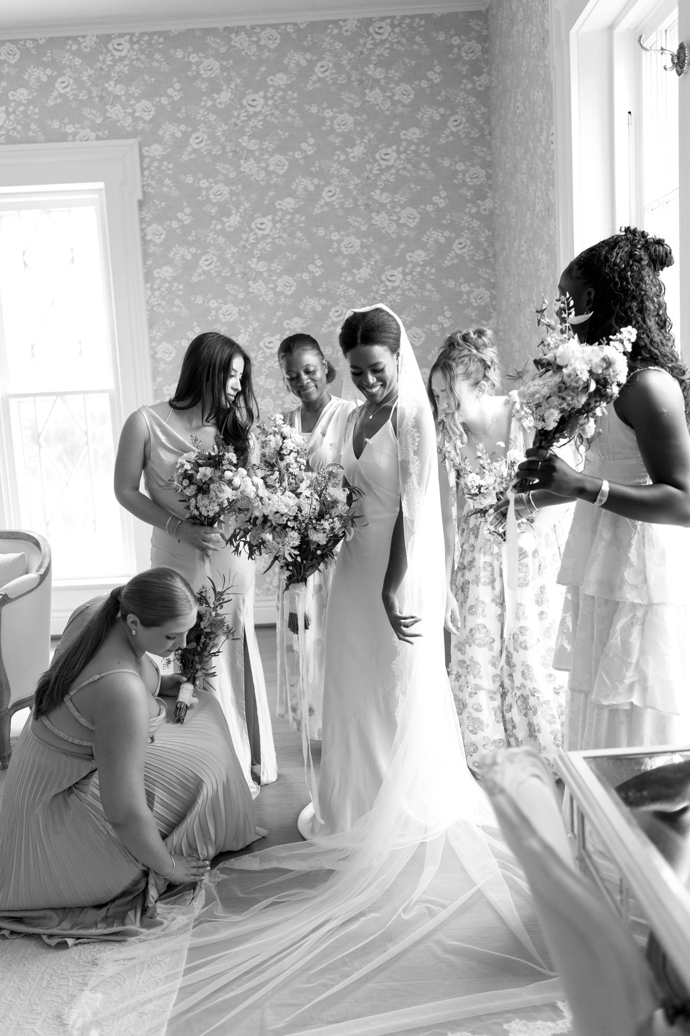 Wedding party in light dresses reacts joyfully during bridal preparation.