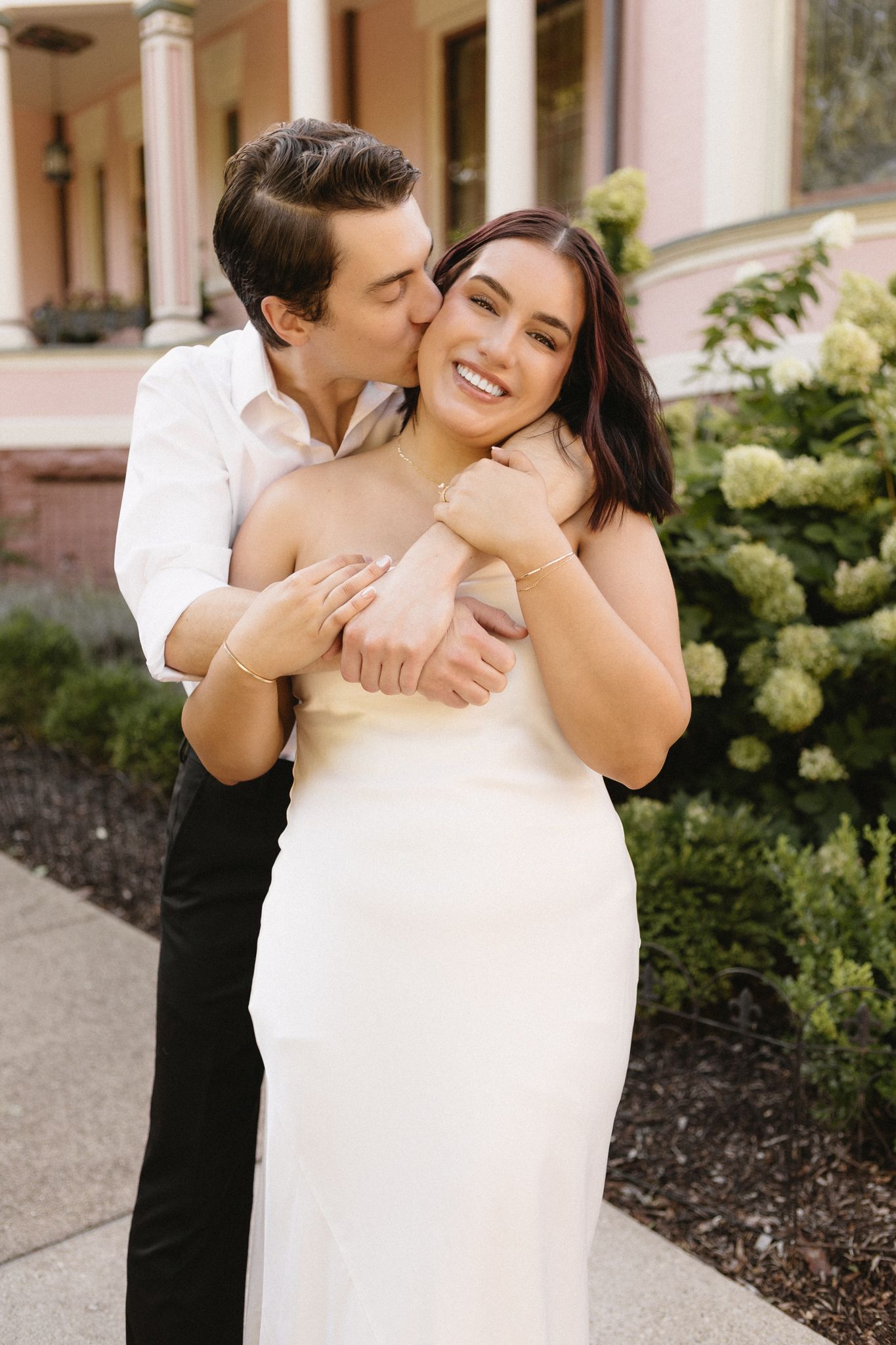 Romantic couple embraces in a garden setting with white hydrangeas in the background.
