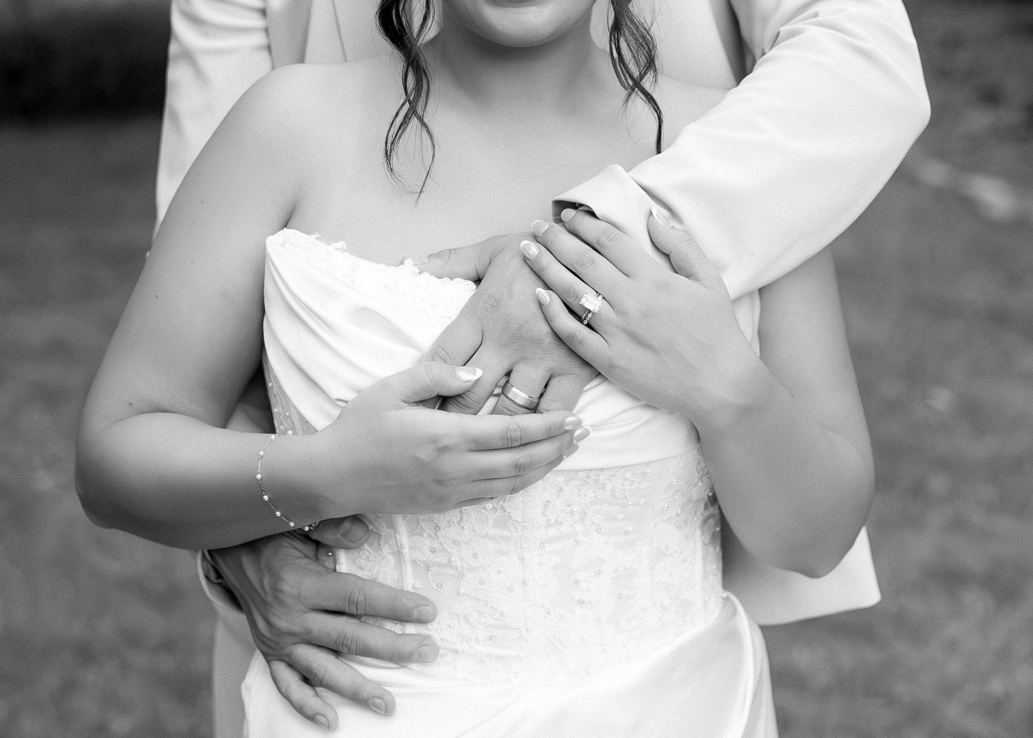 Black and white wedding photo of bride and groom embracing, showing their hands with wedding rings.