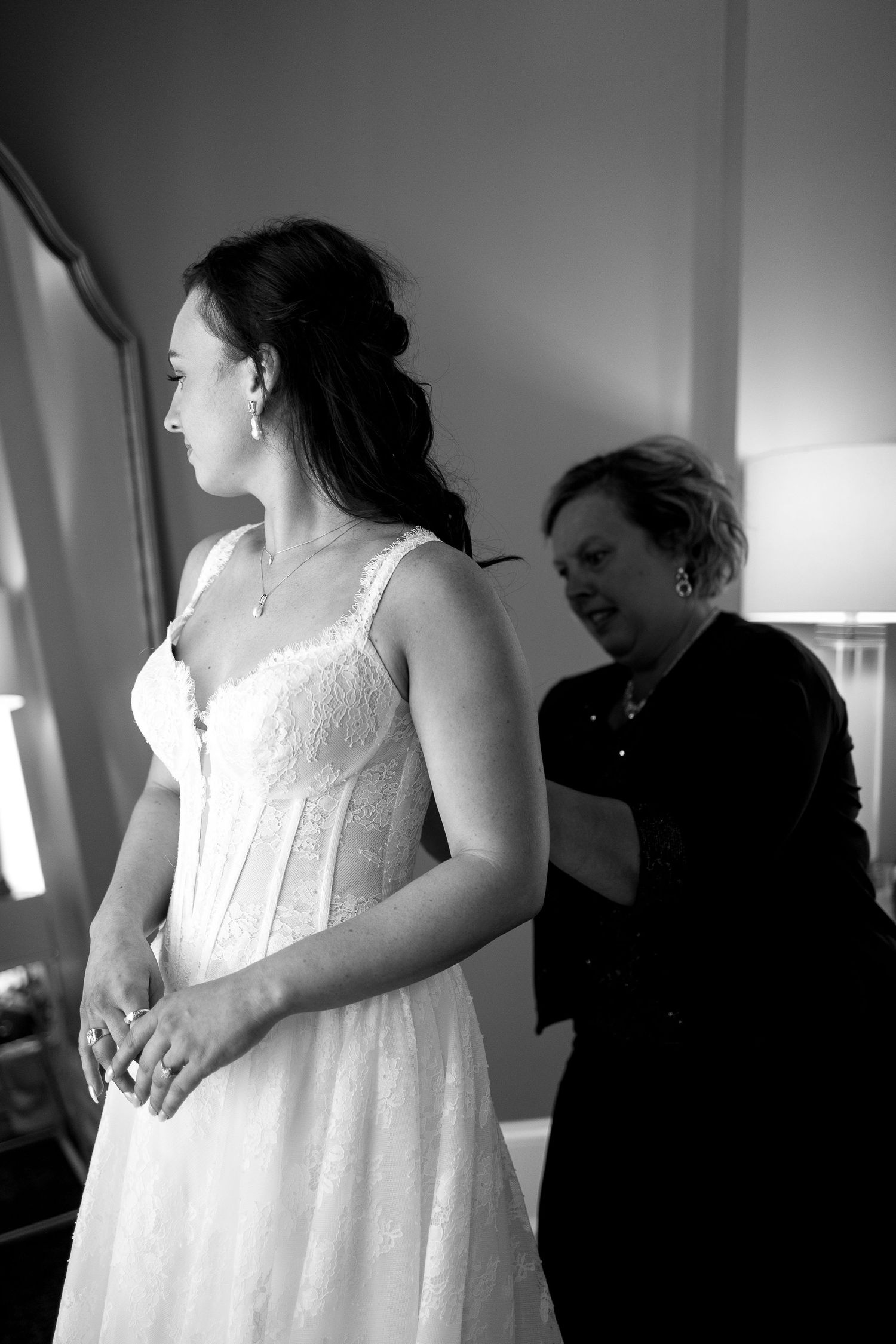 Black and white images capture final wedding dress preparations with helpers.