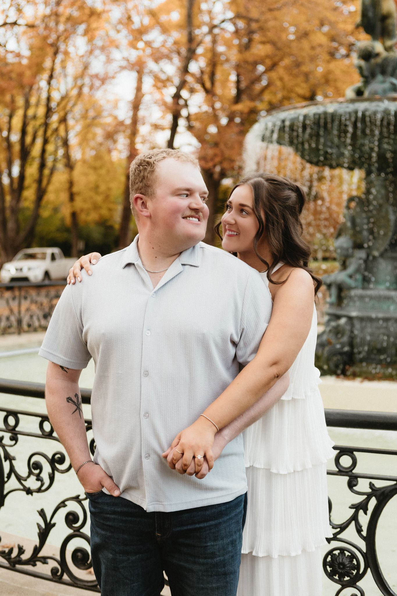 A couple shares intimate moments and laughter near an ornate iron railing during autumn.