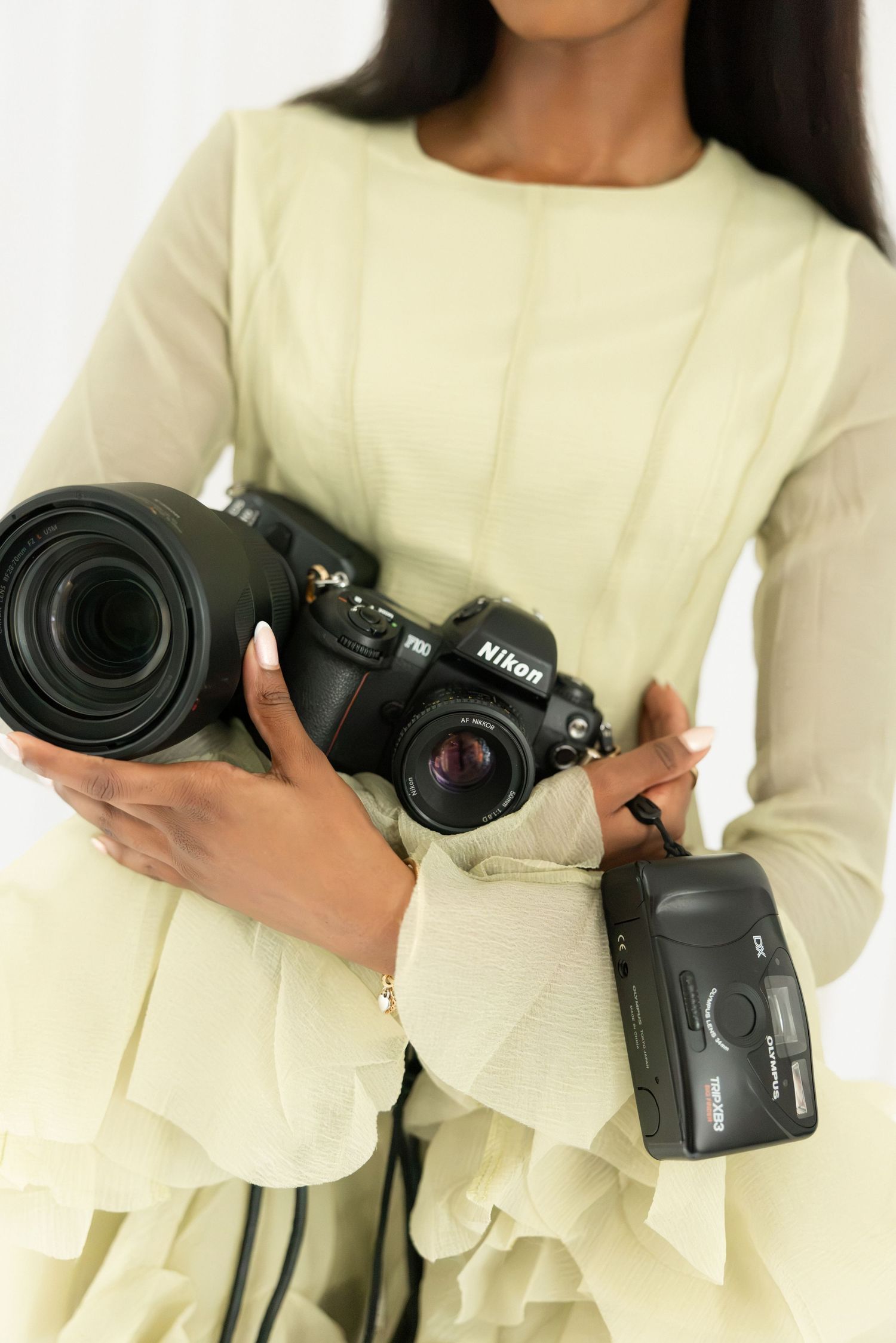 Woman in green dress holding a Nikon DSLR camera with large lens and a compact film camera.