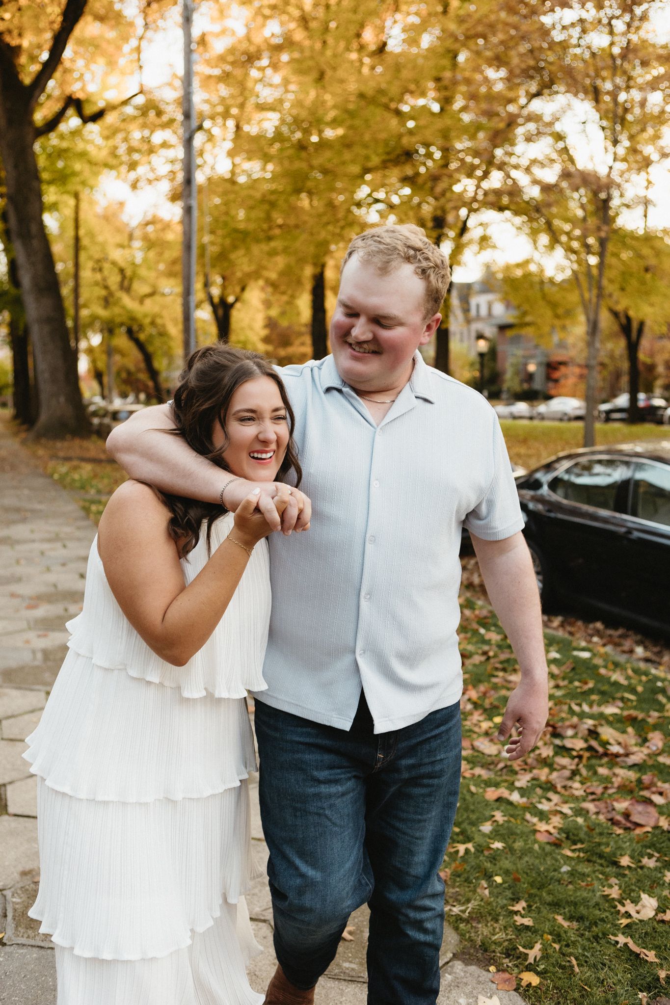 A couple shares joyful moments on an autumn day with golden leaves and trees in the background.