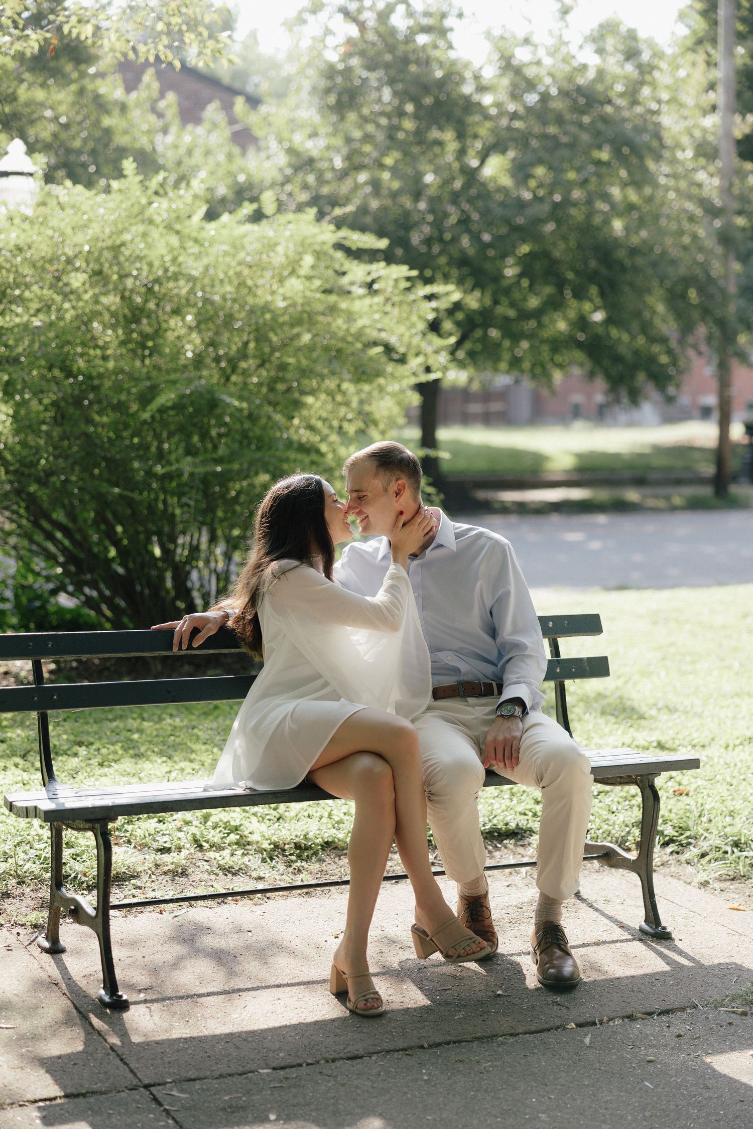 Couple sharing a romantic moment on a park bench surrounded by lush greenery on a sunny day.