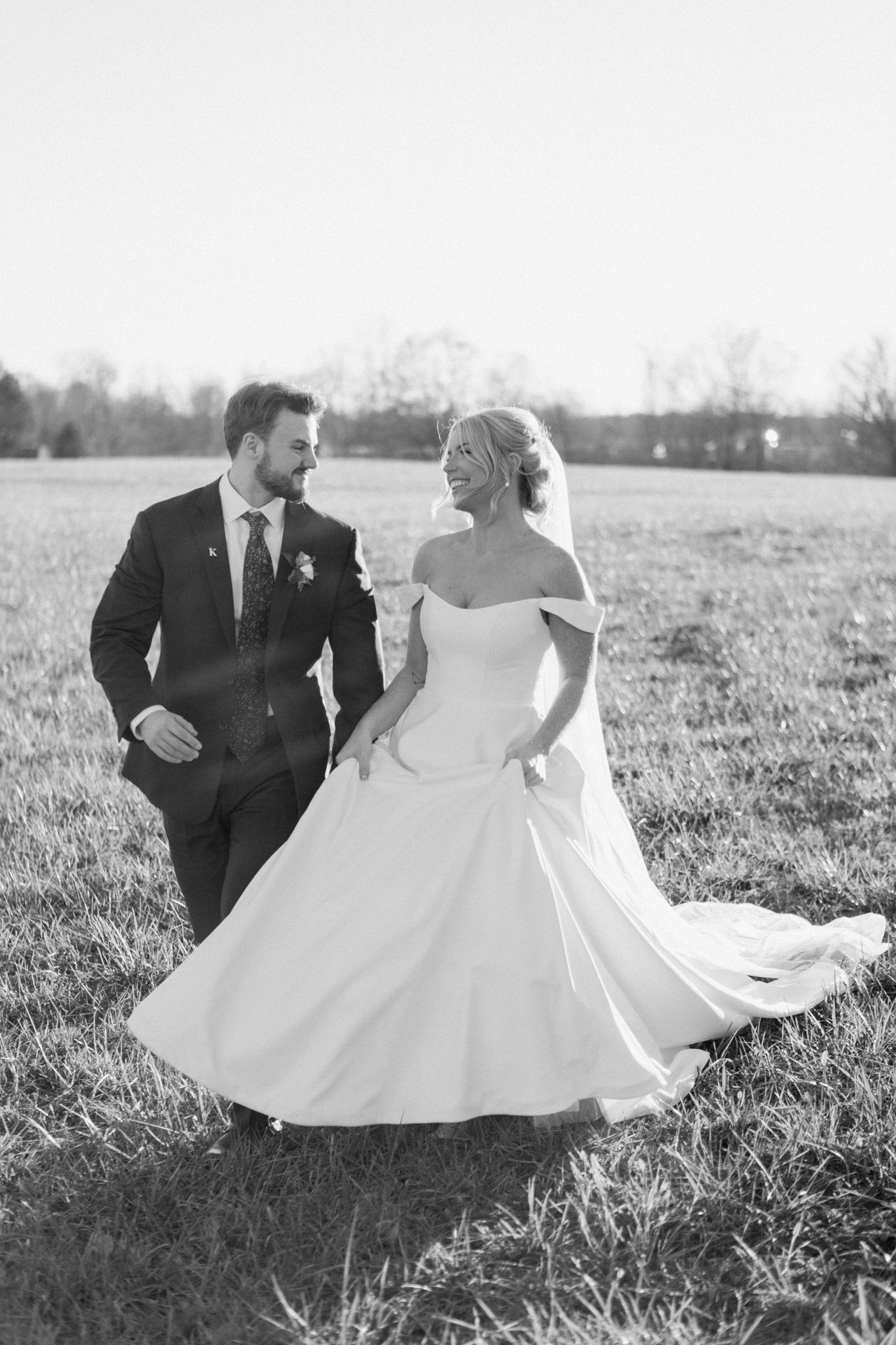 Bride and groom walking through a sunny field at Silo Farms, captured in black and white. Photo by Joia Lyn, KY wedding