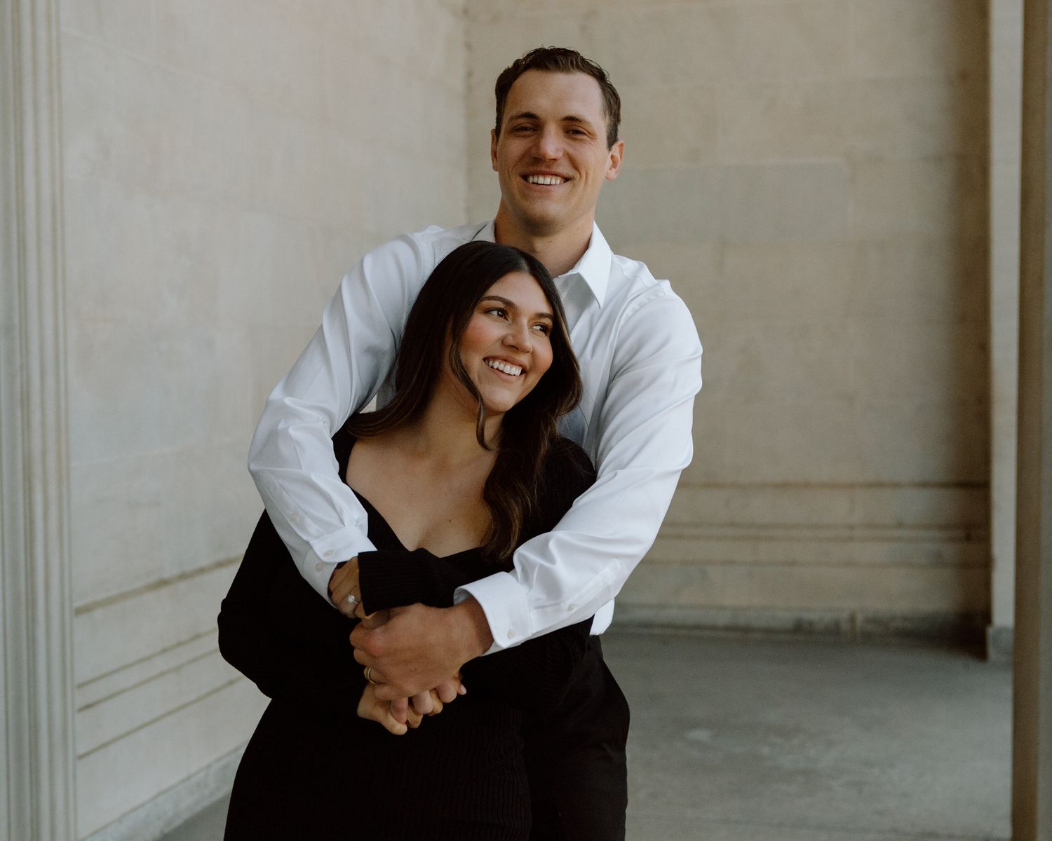 Engaged couple in downtown Louisville, with the woman smiling and showing her engagement ring while embracing her fiancé