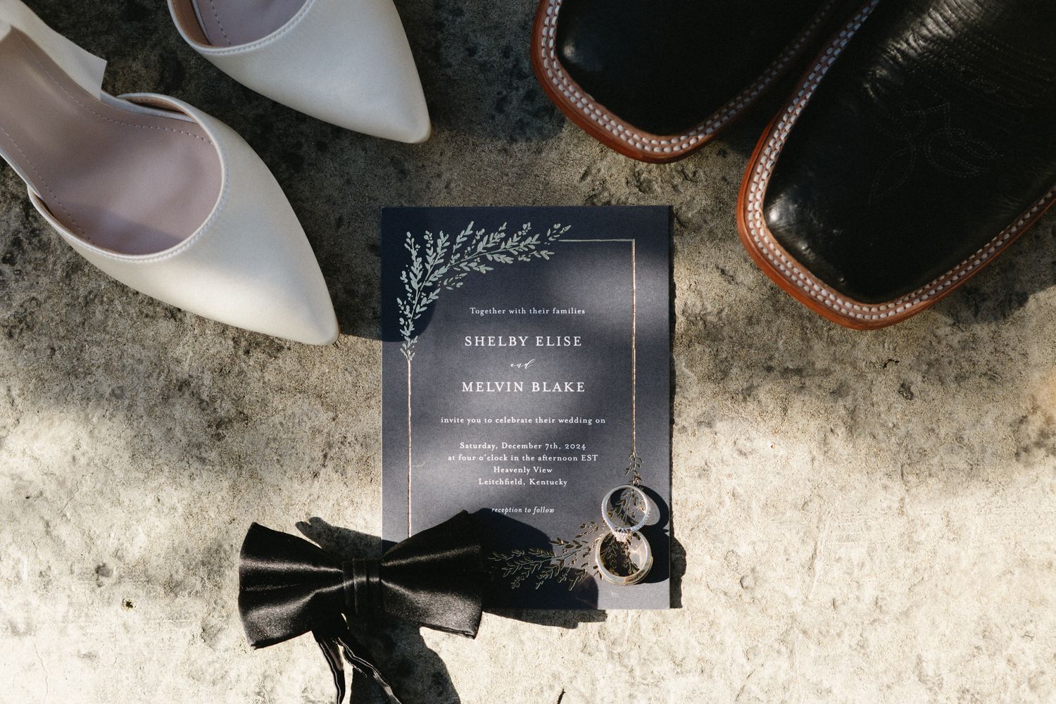 Black leather dress shoes and invitation cards arranged artistically on a textured gray surface.