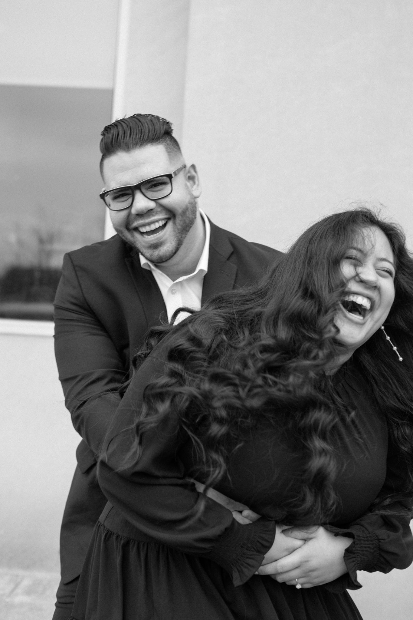 Engaged couple in downtown Louisville, with the woman smiling and showing her engagement ring while embracing her fiancé