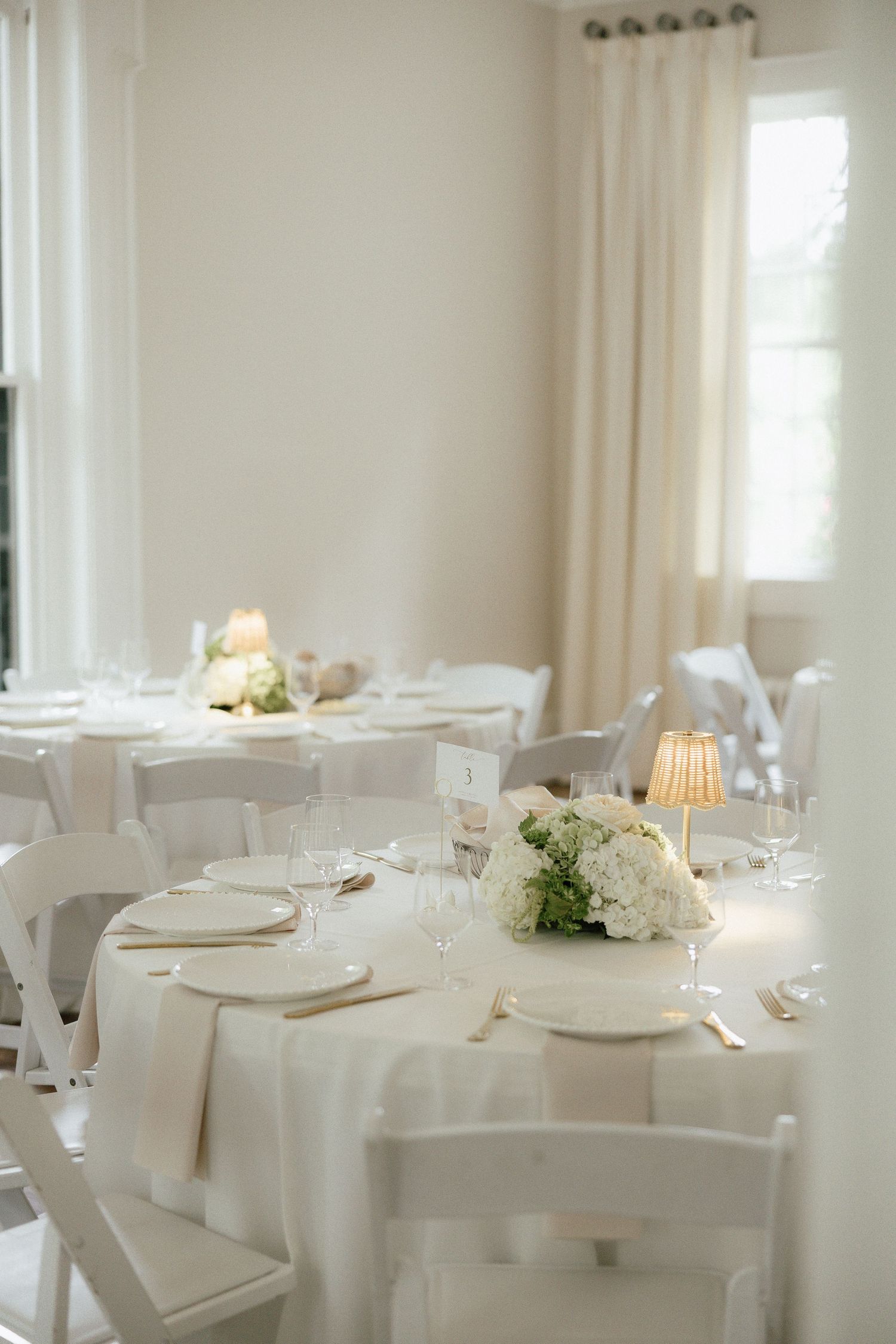 Elegant white wedding reception tables with floral centerpieces, candles, and glassware.