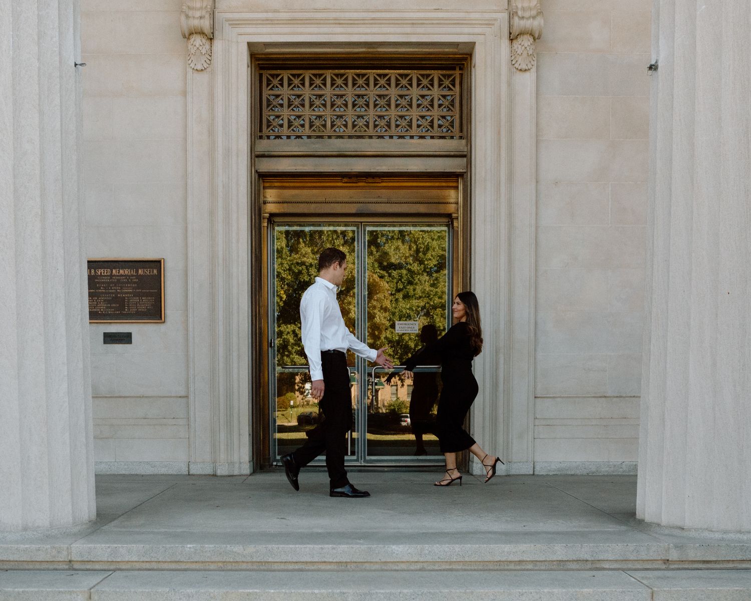 Engaged couple in downtown Louisville, with the woman smiling and showing her engagement ring while embracing her fiancé