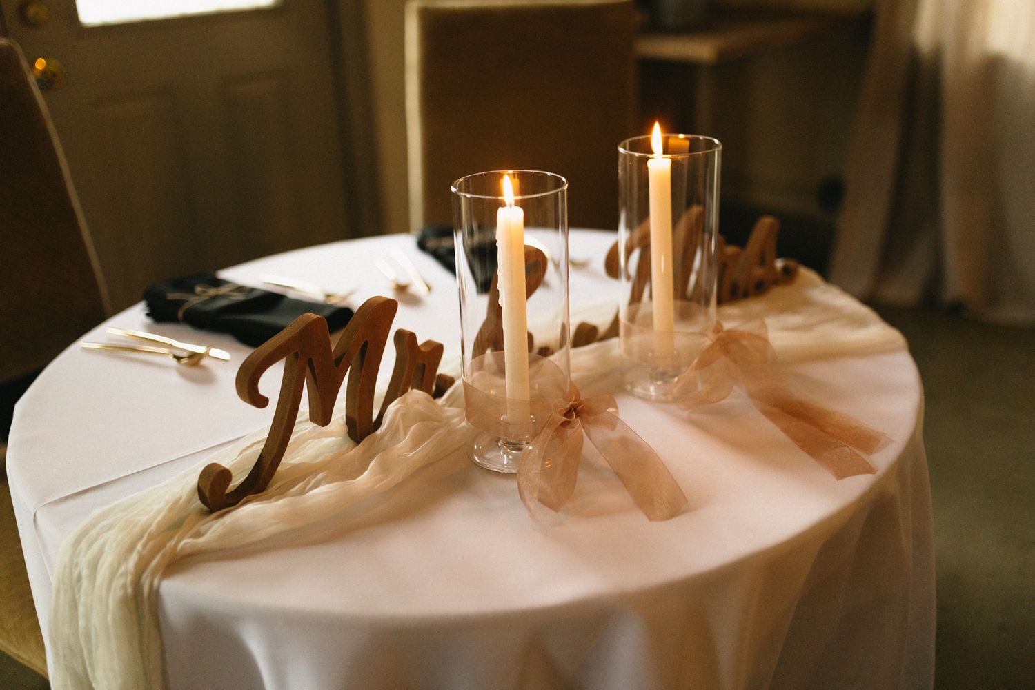 A wedding reception table decorated with glowing white candles and elegant 'Mr.' signage on white linen tablecloth.