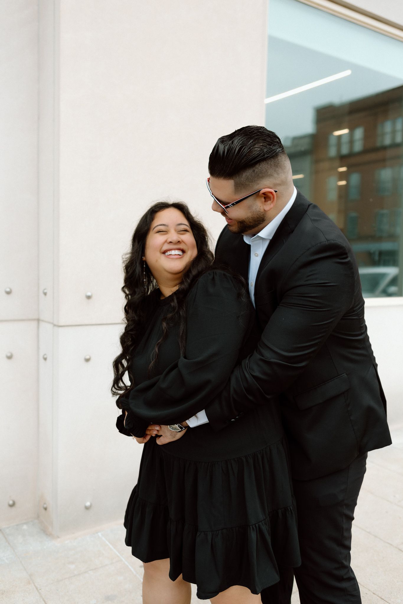 Engaged couple in downtown Louisville, with the woman smiling and showing her engagement ring while embracing her fiancé