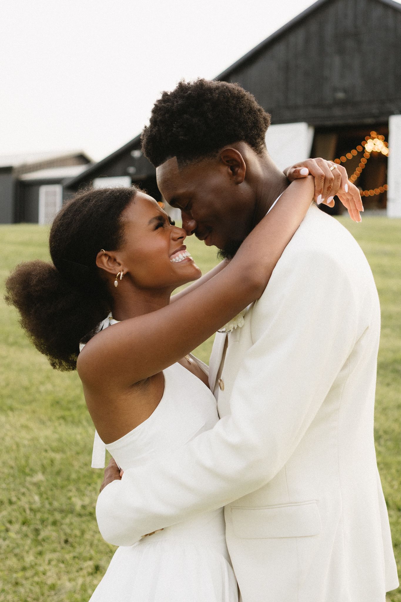 A joyful wedding couple shares an intimate moment while embracing in front of a barn.