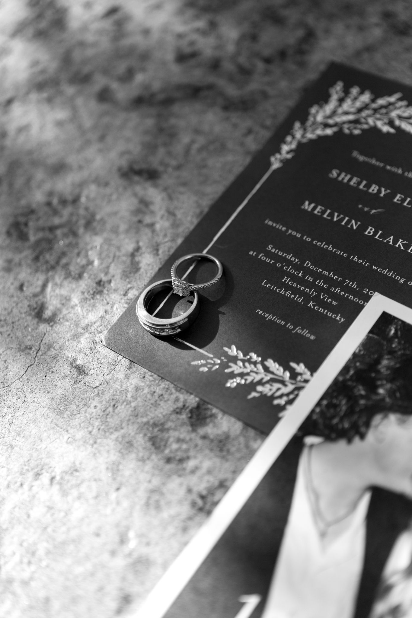 Black luxury wedding invitations with elegant white text and wedding rings displayed on textured surface.