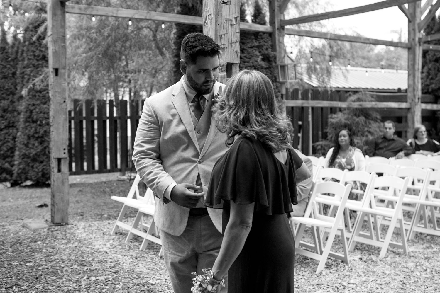A tender black and white moment between a couple at an outdoor venue with white folding chairs in the background.