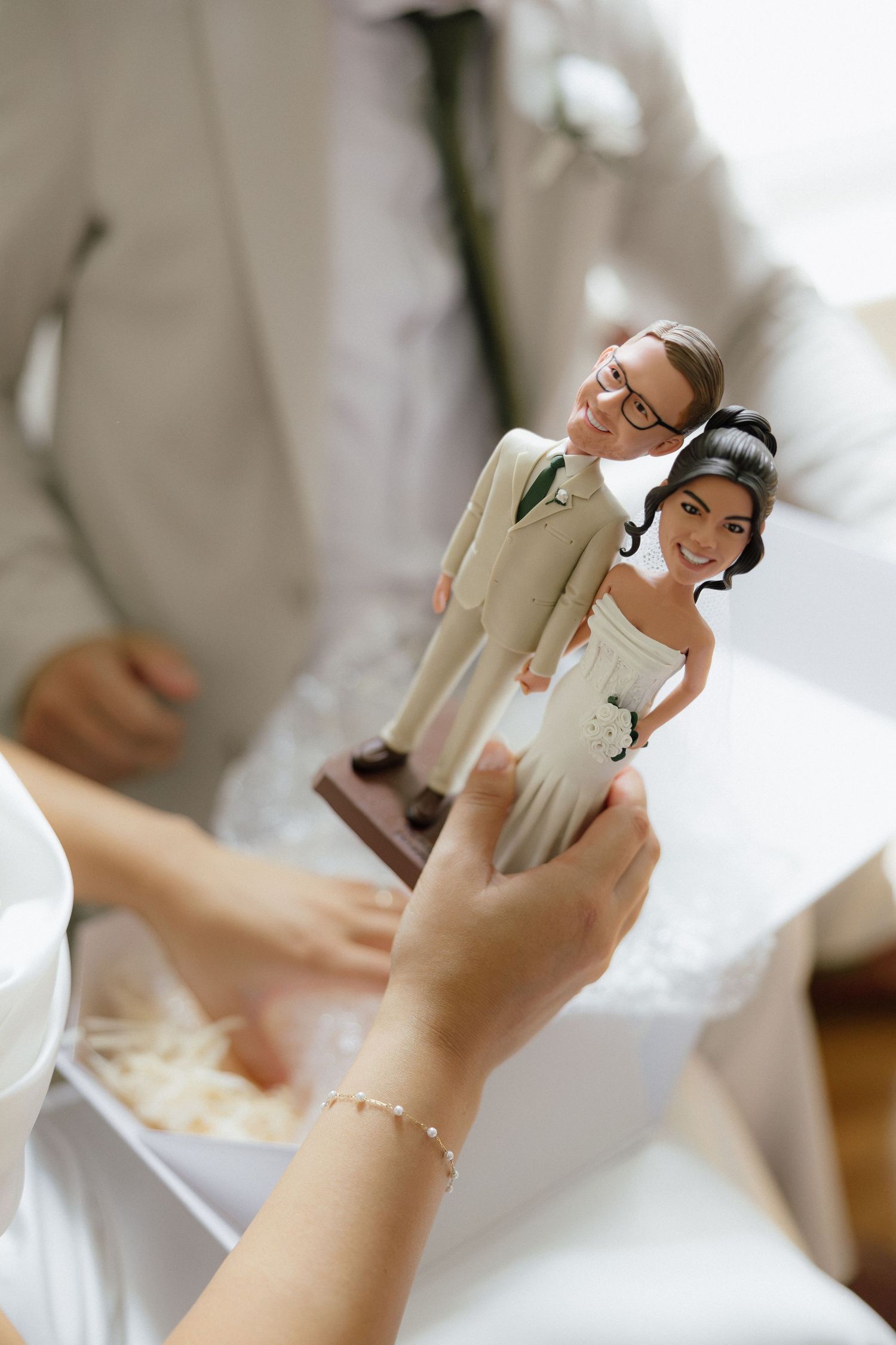 Custom wedding cake topper figurines resembling the bride and groom being held up for display.