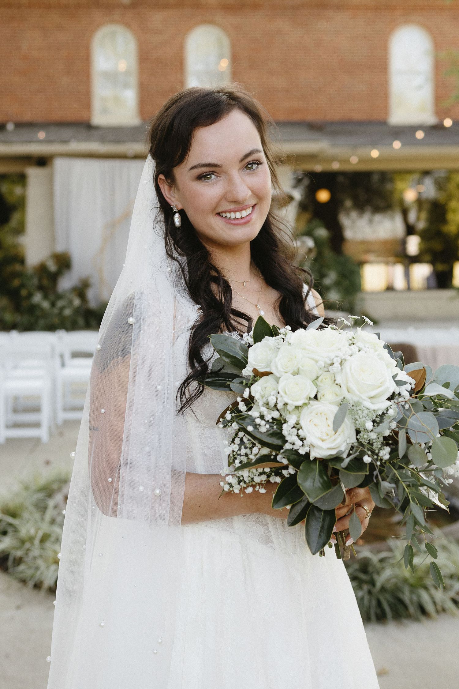 A close-up bridal portrait showcasing a white bouquet with eucalyptus and a flowing veil.
