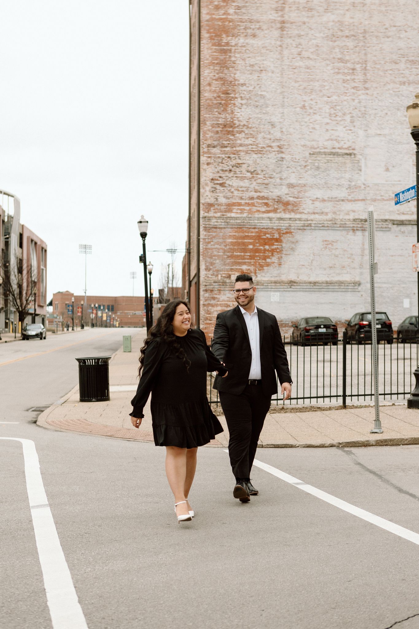 Elegant engaged couple smiling and embracing in downtown Louisville, with the woman showing her engagement ring