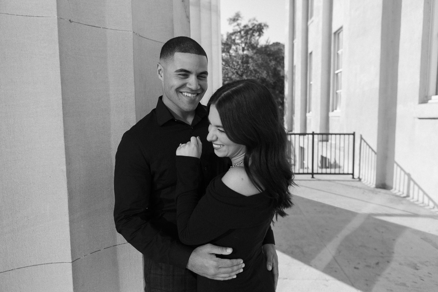 A romantic black and white portrait of a couple embracing on an elegant columned porch.