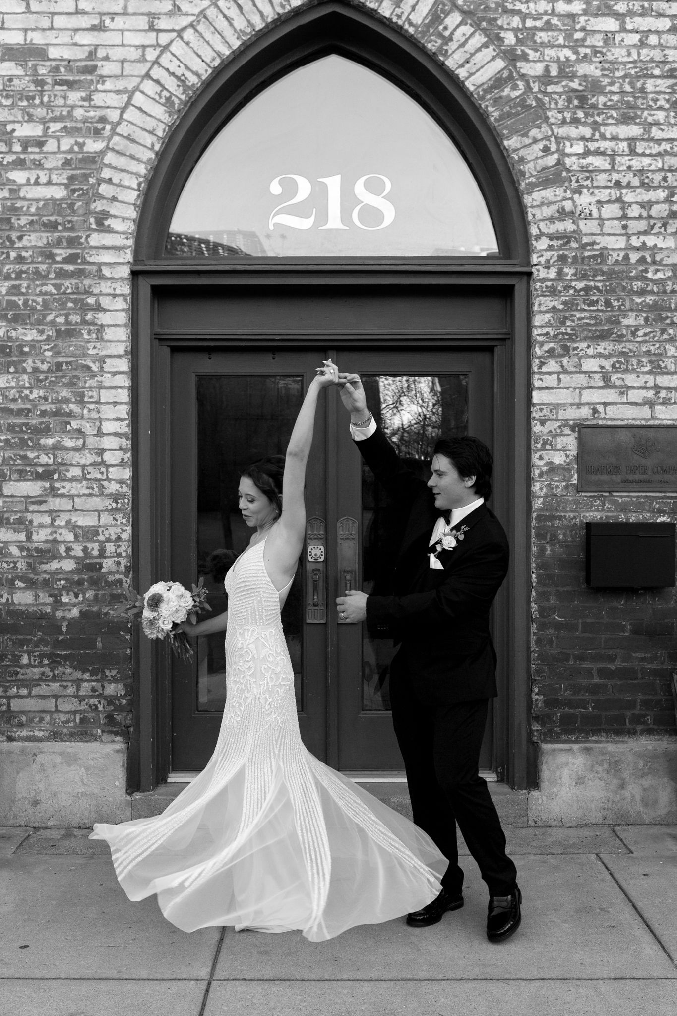 A couple dancing in front of building number 218 with an arched doorway, shown in black and white.