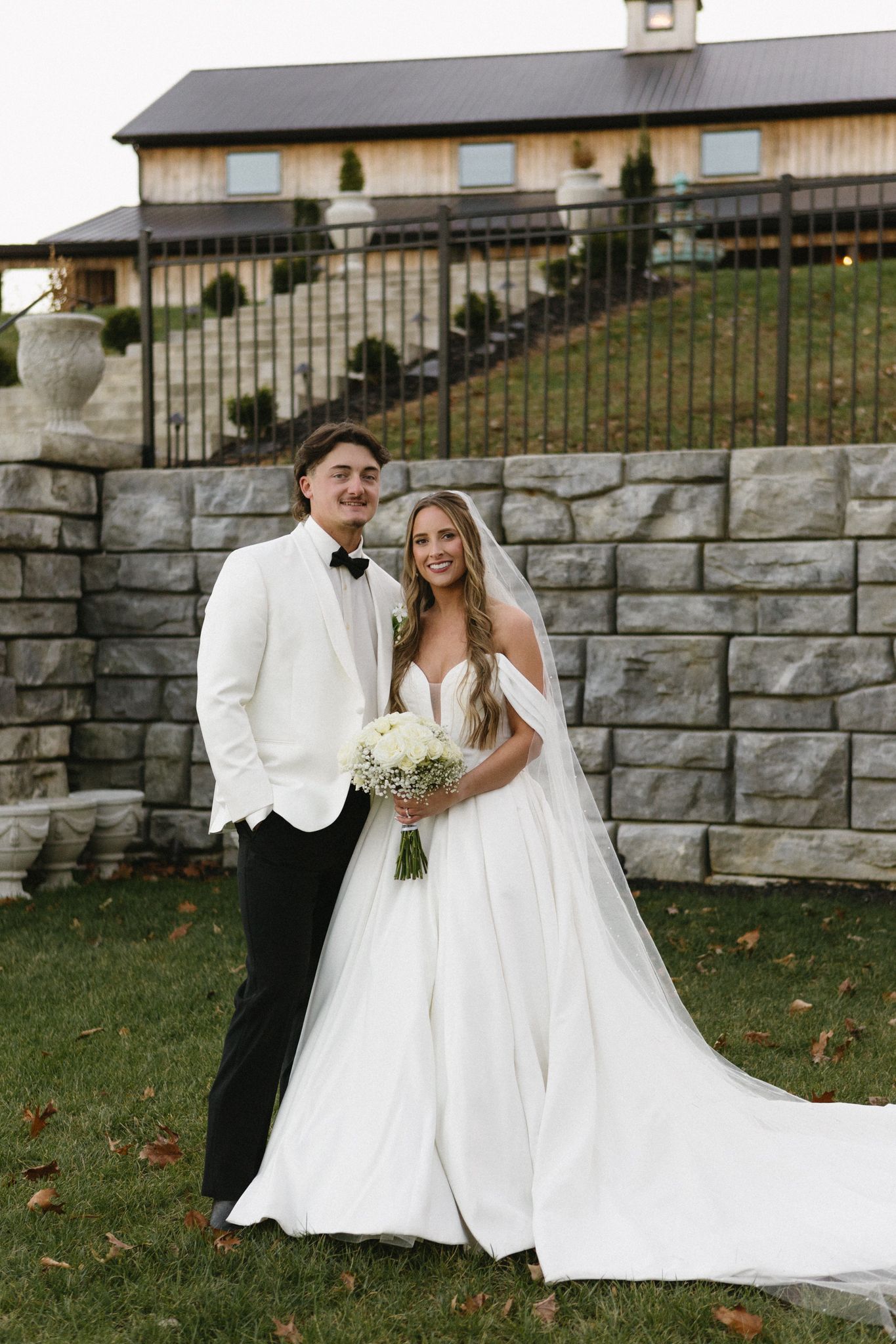Wedding couple poses in front of a stone wall backdrop at their venue.