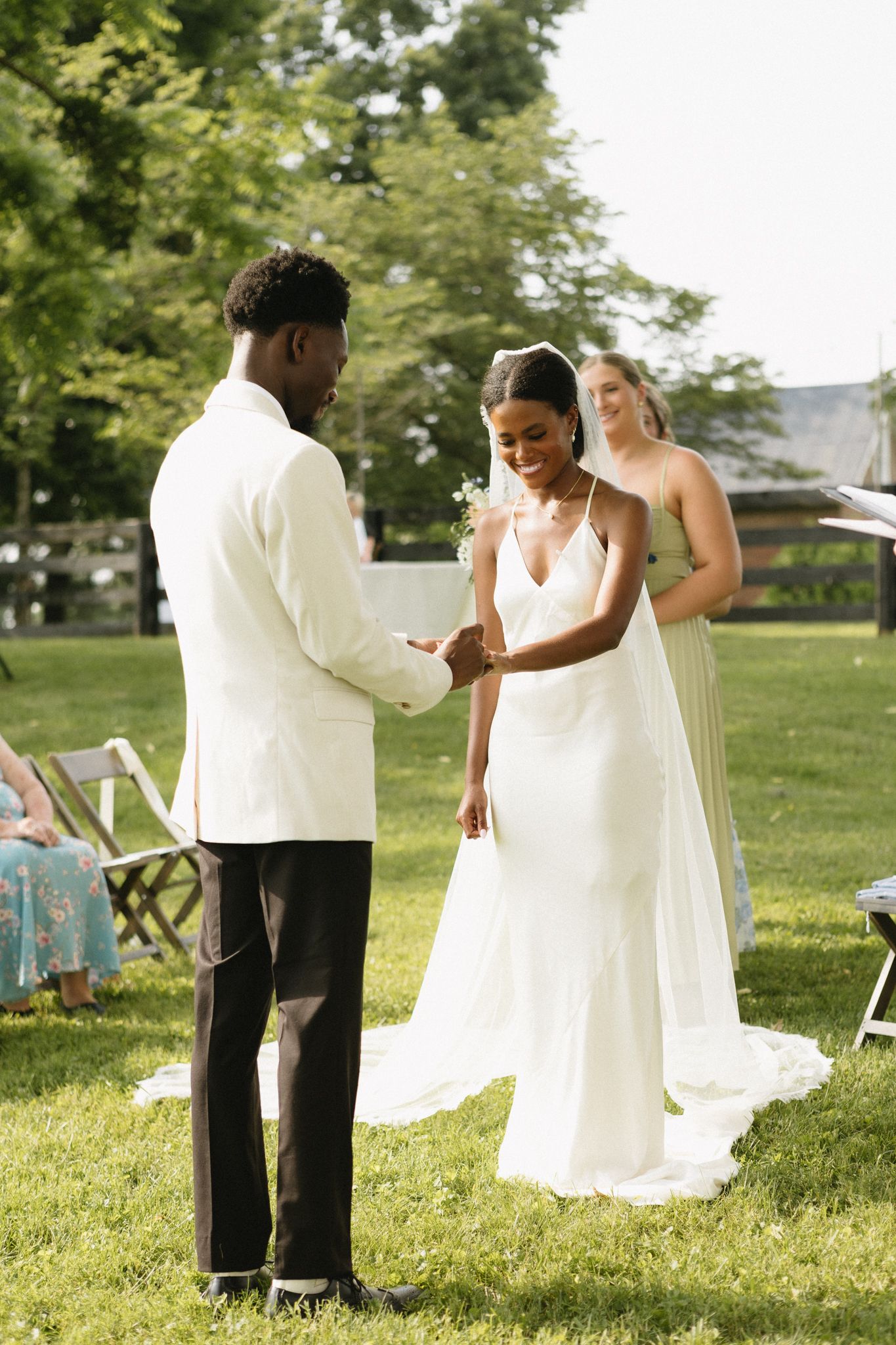 Wedding party members in coordinated outfits share a celebratory dance moment on grass.