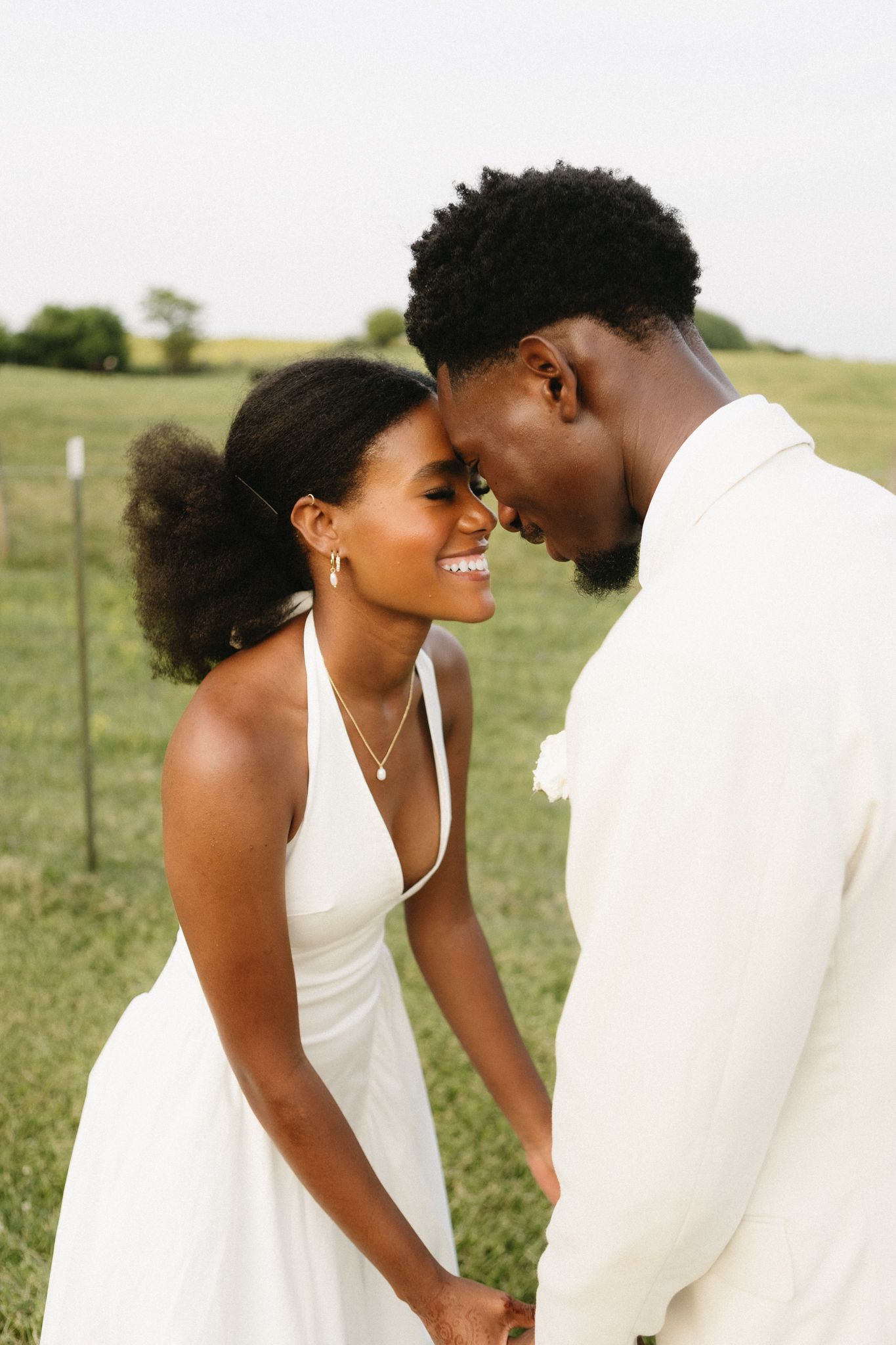 A couple in white formal attire share intimate moments in a romantic outdoor photoshoot.