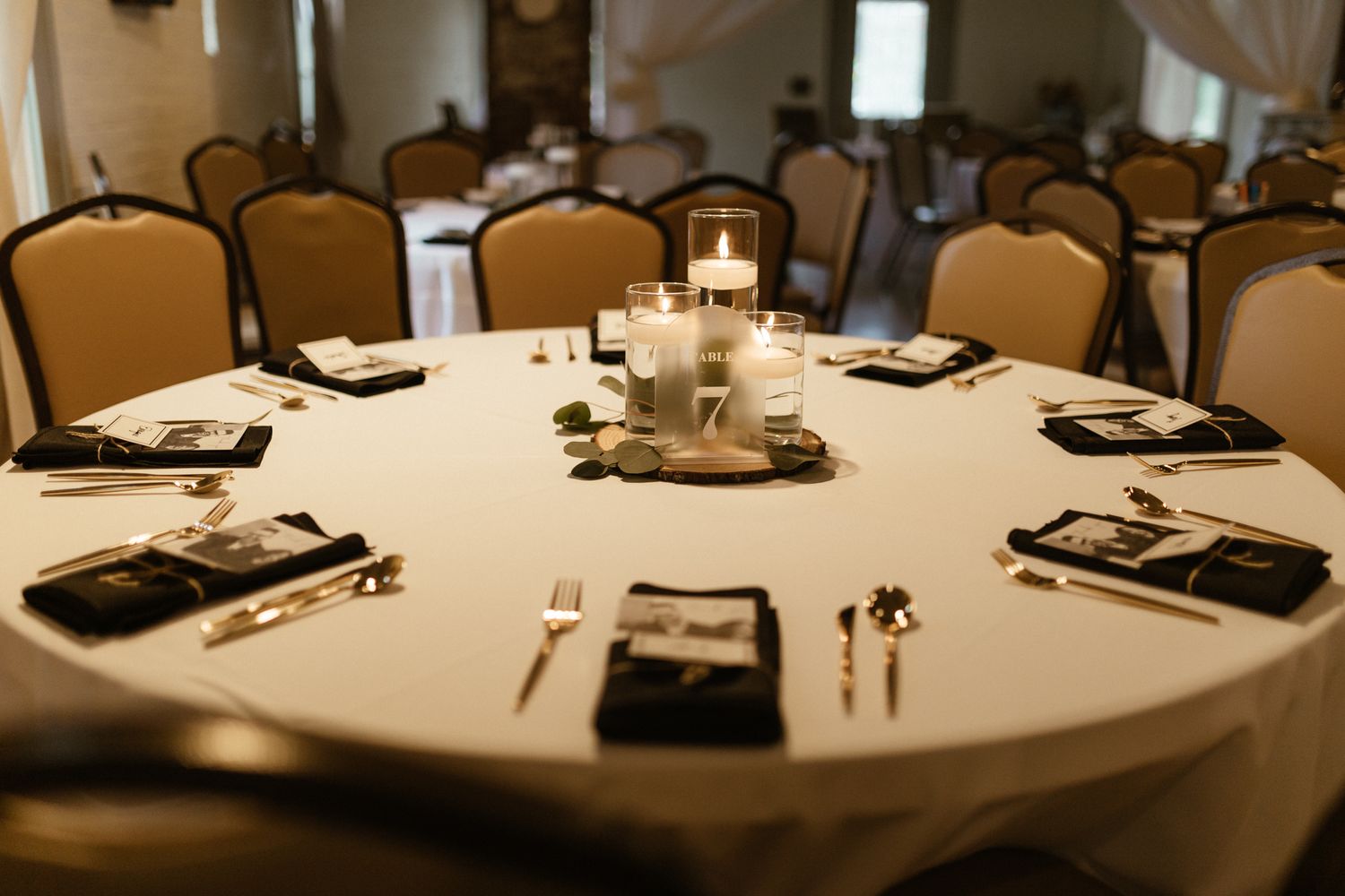 Elegant round dining table set with black placemats, silverware and centerpieces in formal banquet setting.