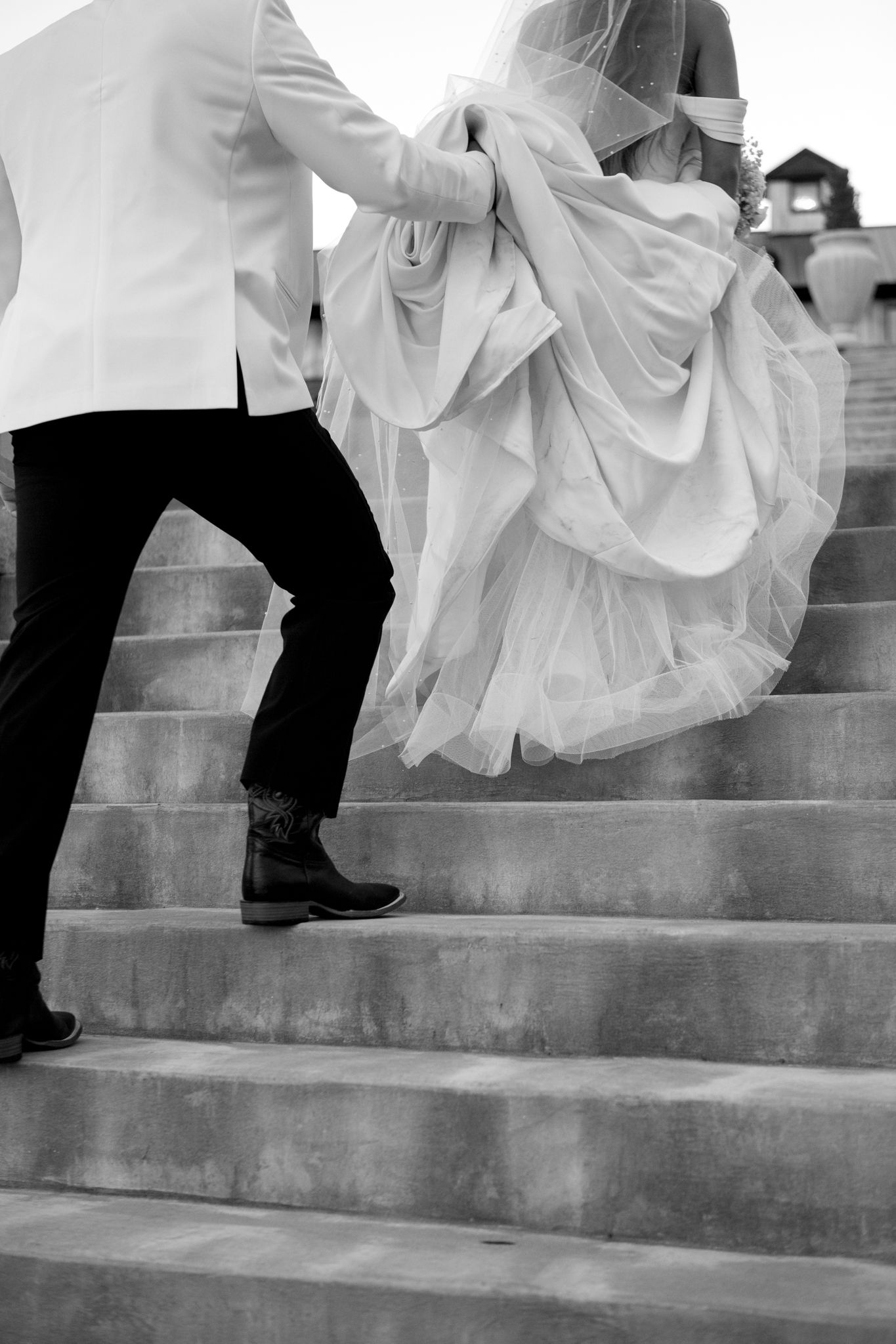 Black and white photo of a bride's dress flowing down stone steps.