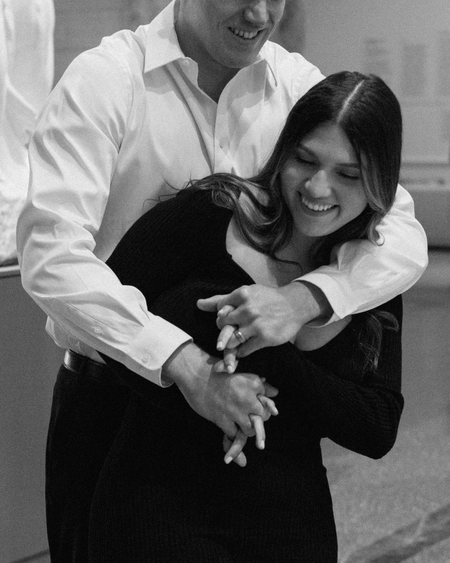 Engaged couple in downtown Louisville, with the woman smiling and showing her engagement ring while embracing her fiancé