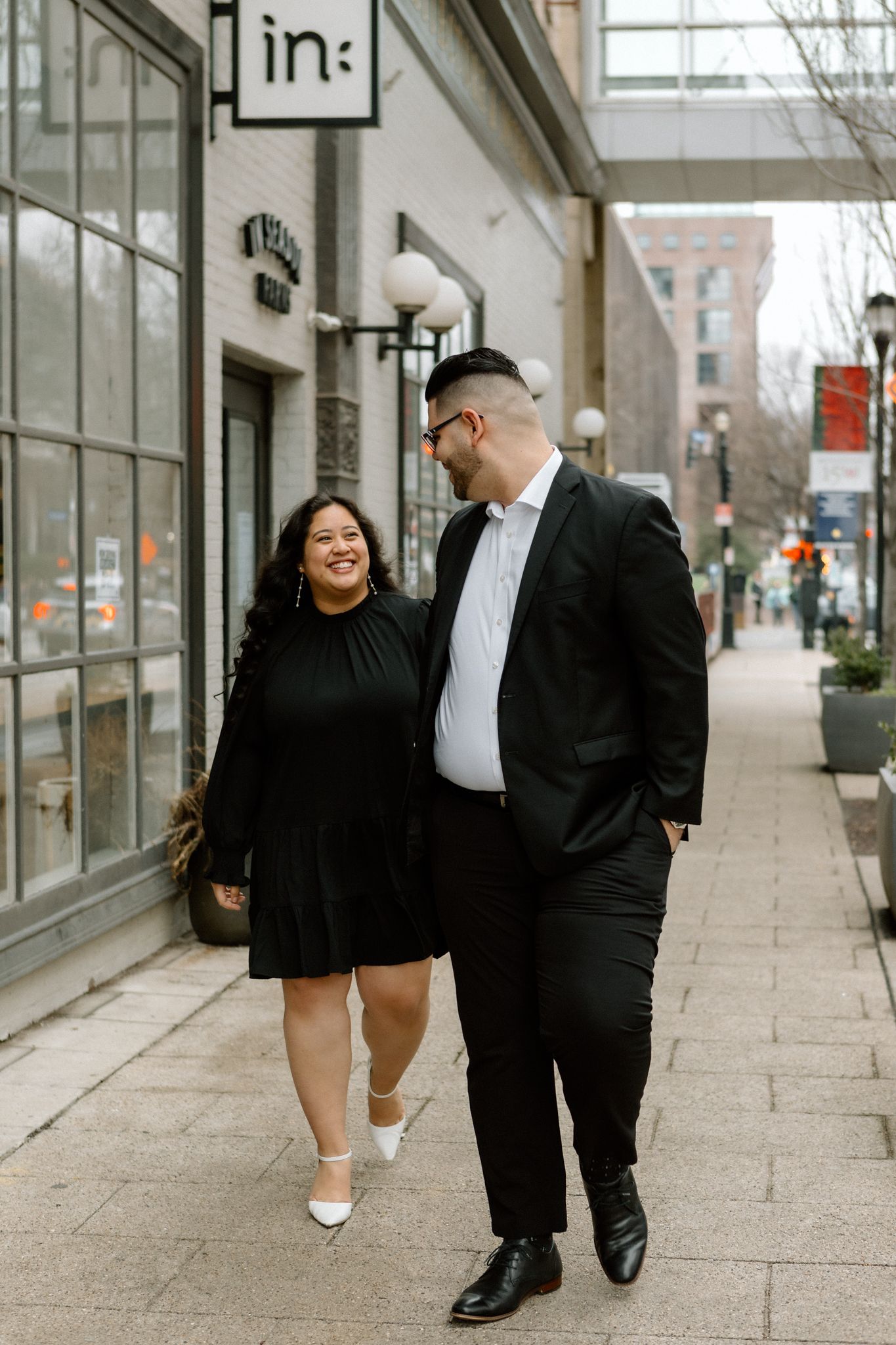 Elegant engaged couple smiling and embracing in downtown Louisville, with the woman showing her engagement ring