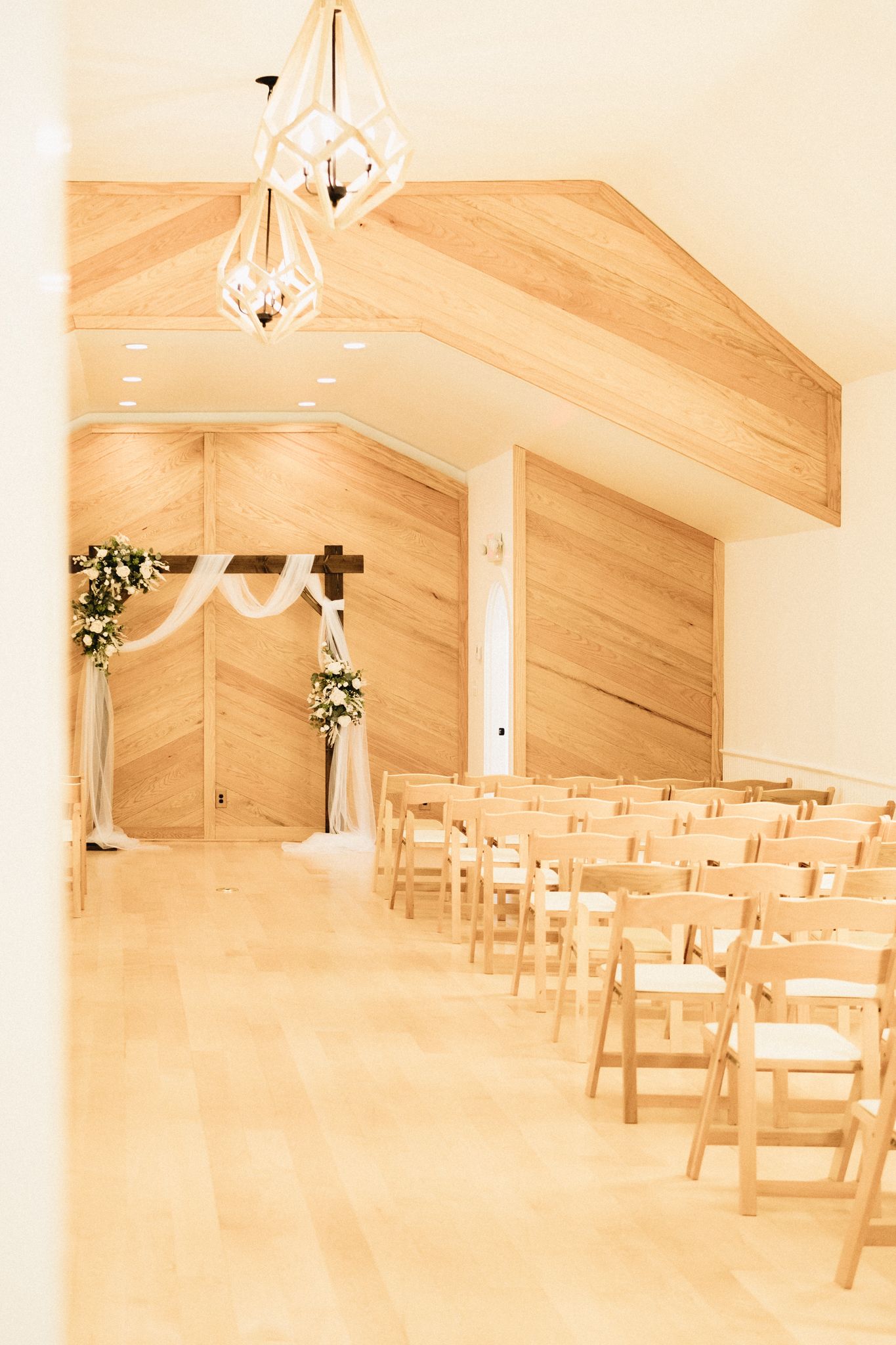 Interior of a rustic wedding chapel with wooden chairs, beamed ceiling, and elegant geometric pendant lights.