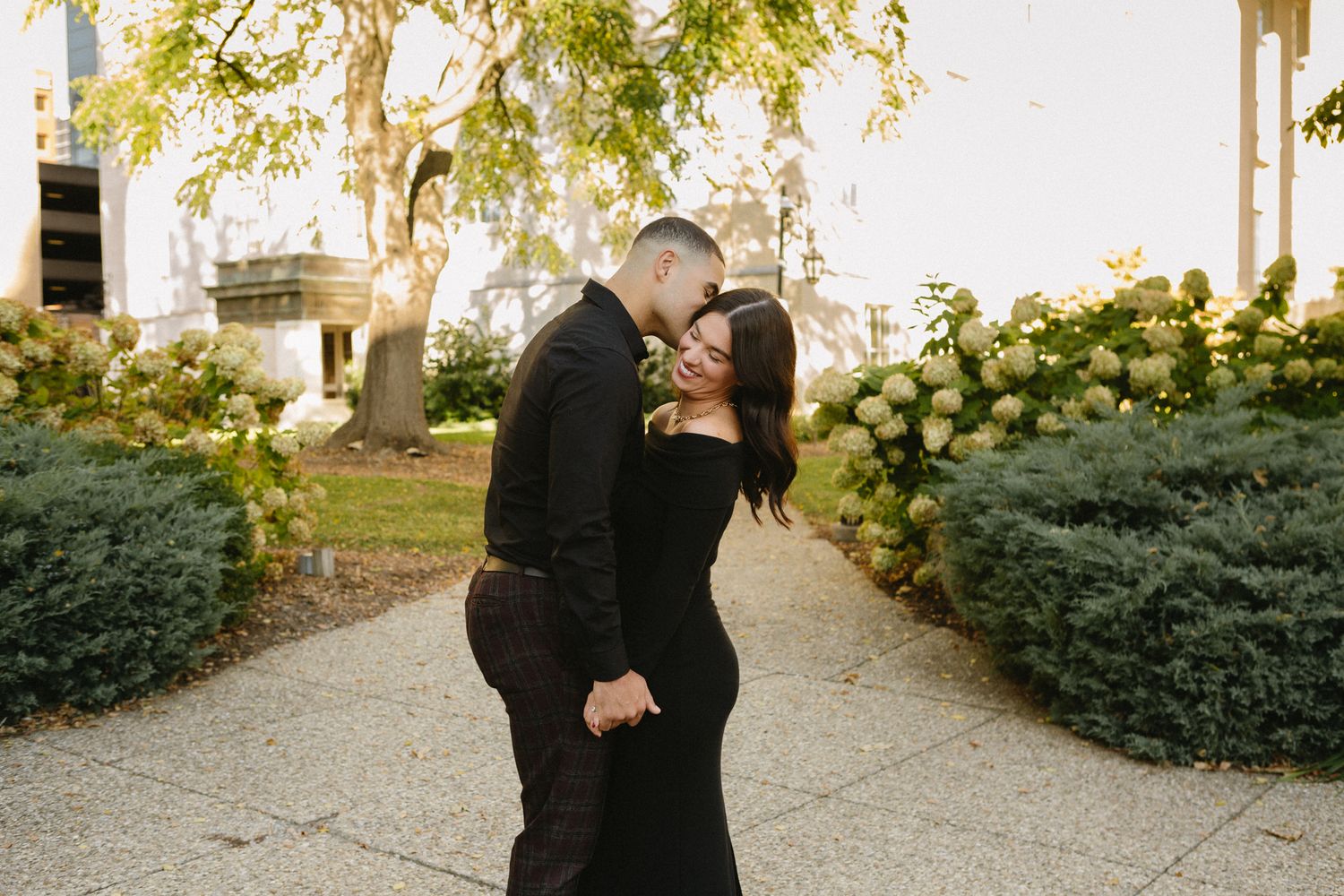 Couple embracing on a garden path surrounded by greenery and sunlight.
