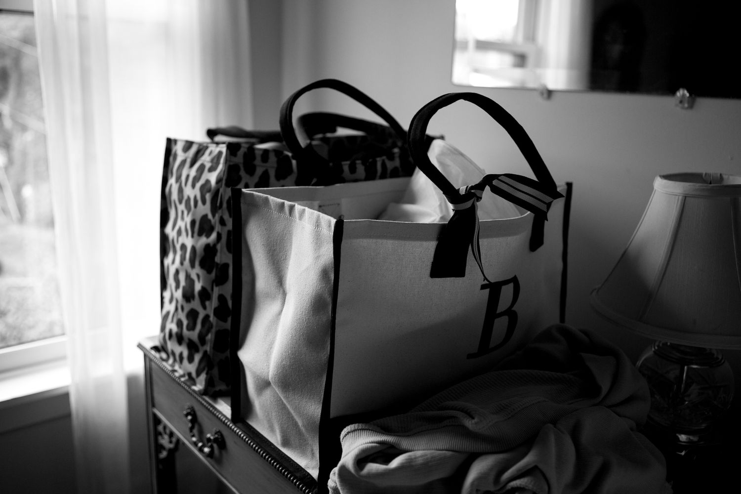 A black and white photograph of handbags and purses arranged on a table near a window.
