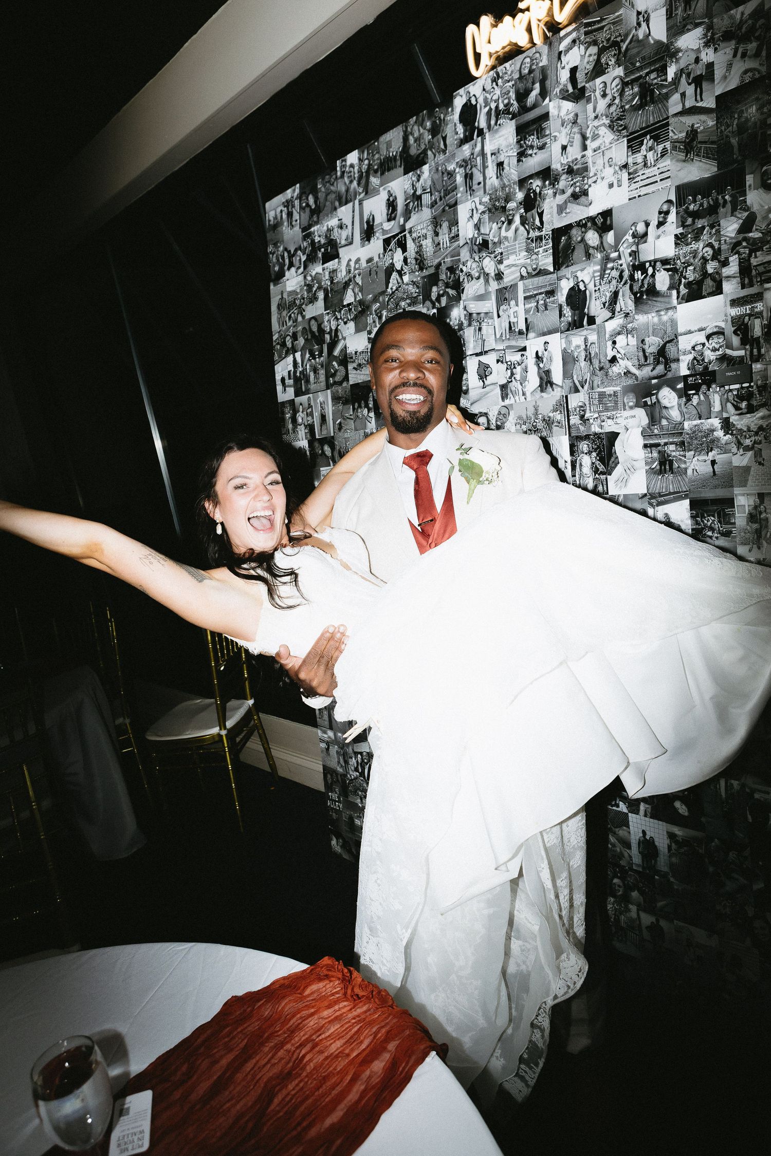 Joyful newlyweds celebrating during their wedding reception against a photo collage wall.