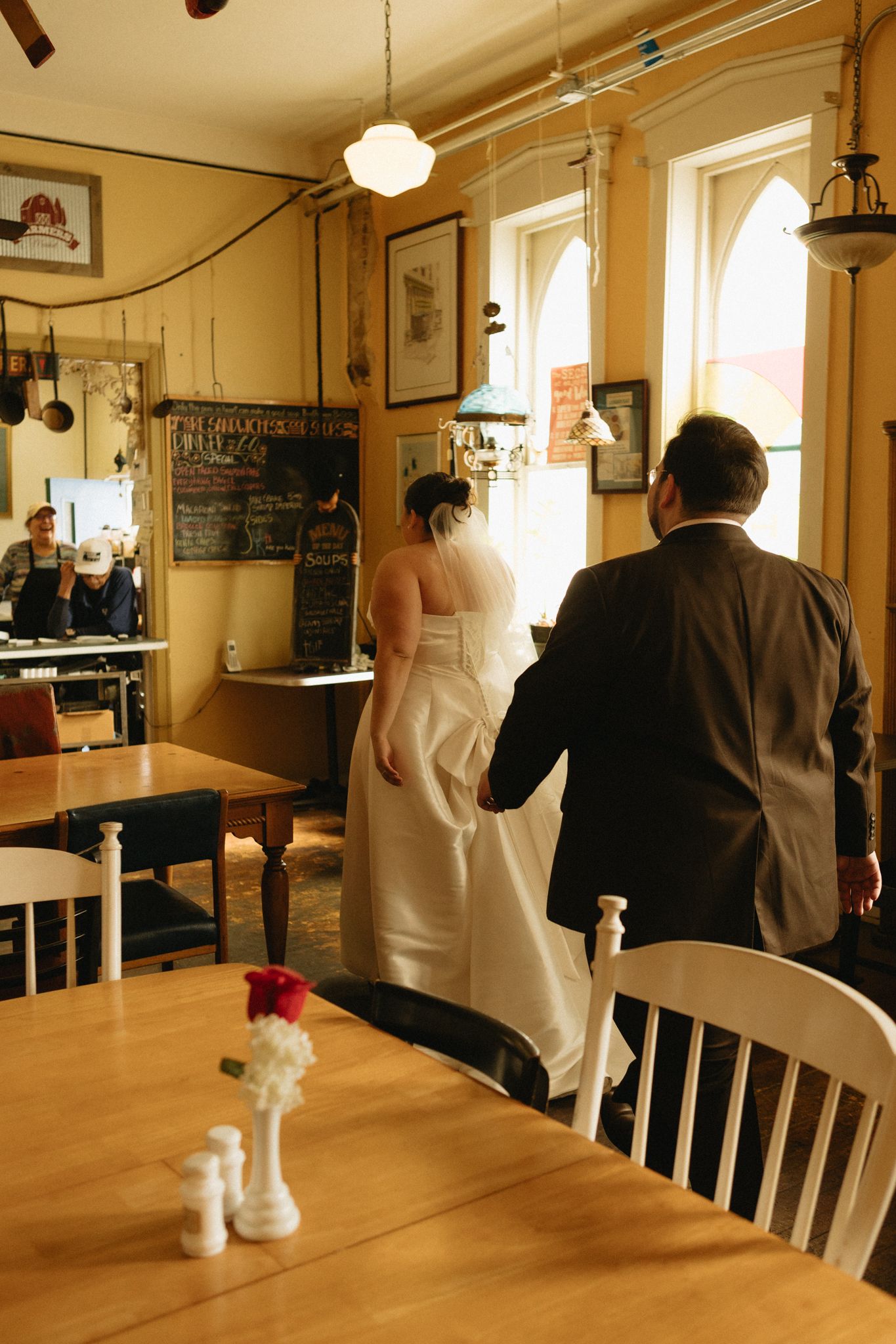 Wedding party walks through a rustic dining room with wooden tables and chairs.