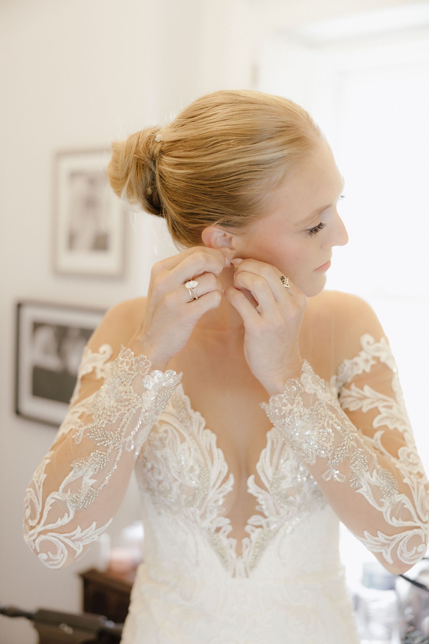 Bride in lace long-sleeve wedding gown putting on earrings while getting ready on her wedding day.
