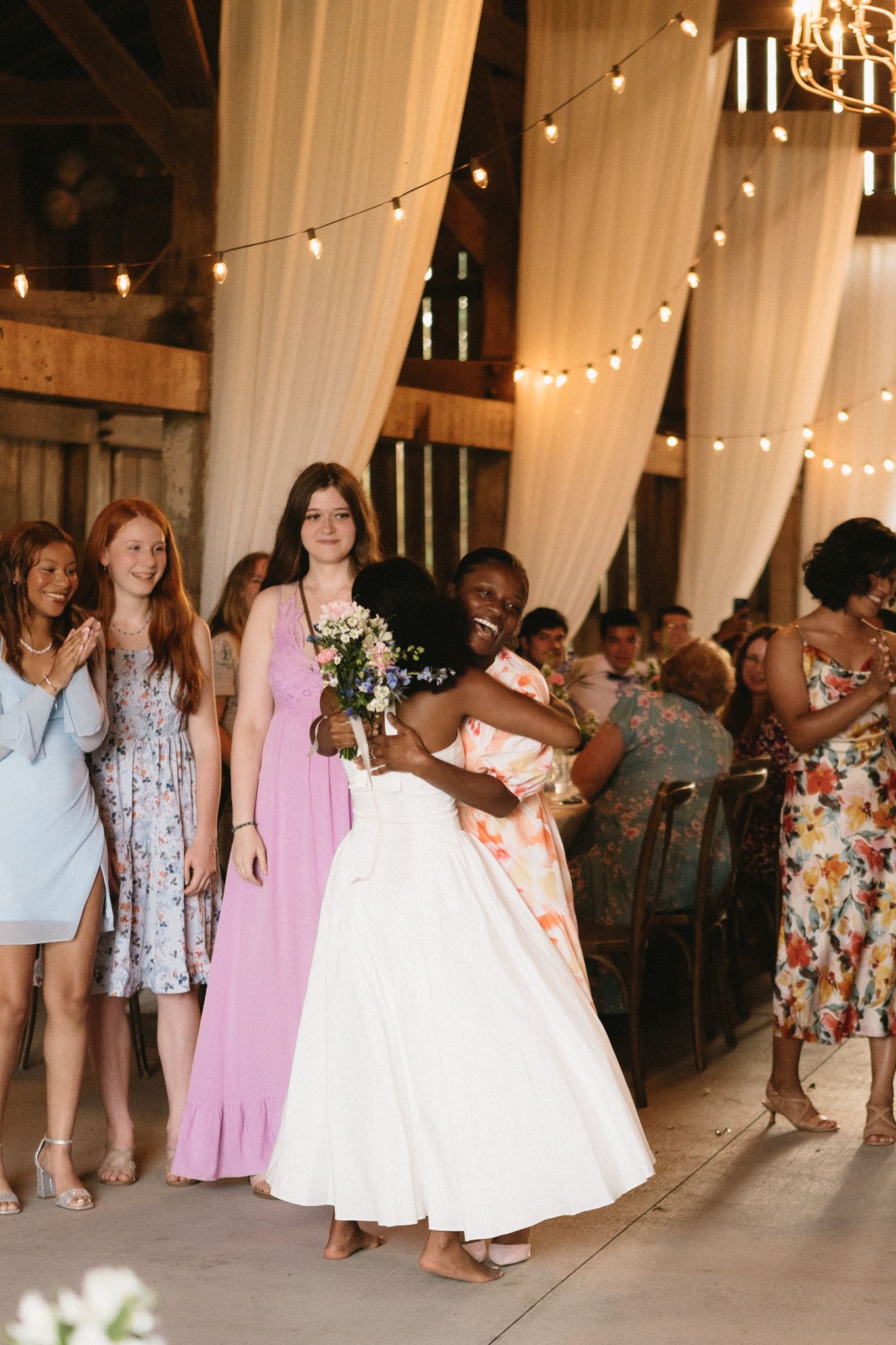 A wedding reception in a rustic barn venue decorated with string lights and white drapes.