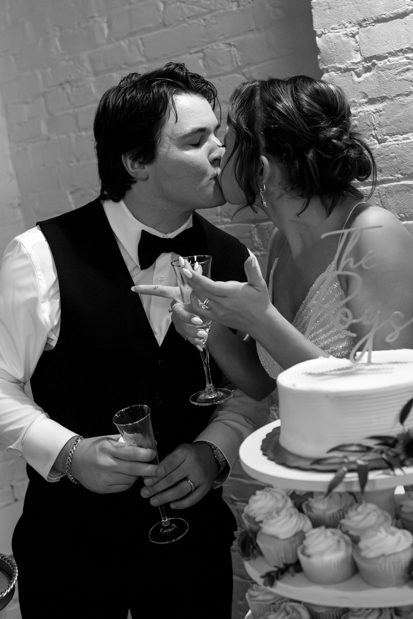 Newlywed couple in black and white sharing a romantic moment with champagne and wedding cake.