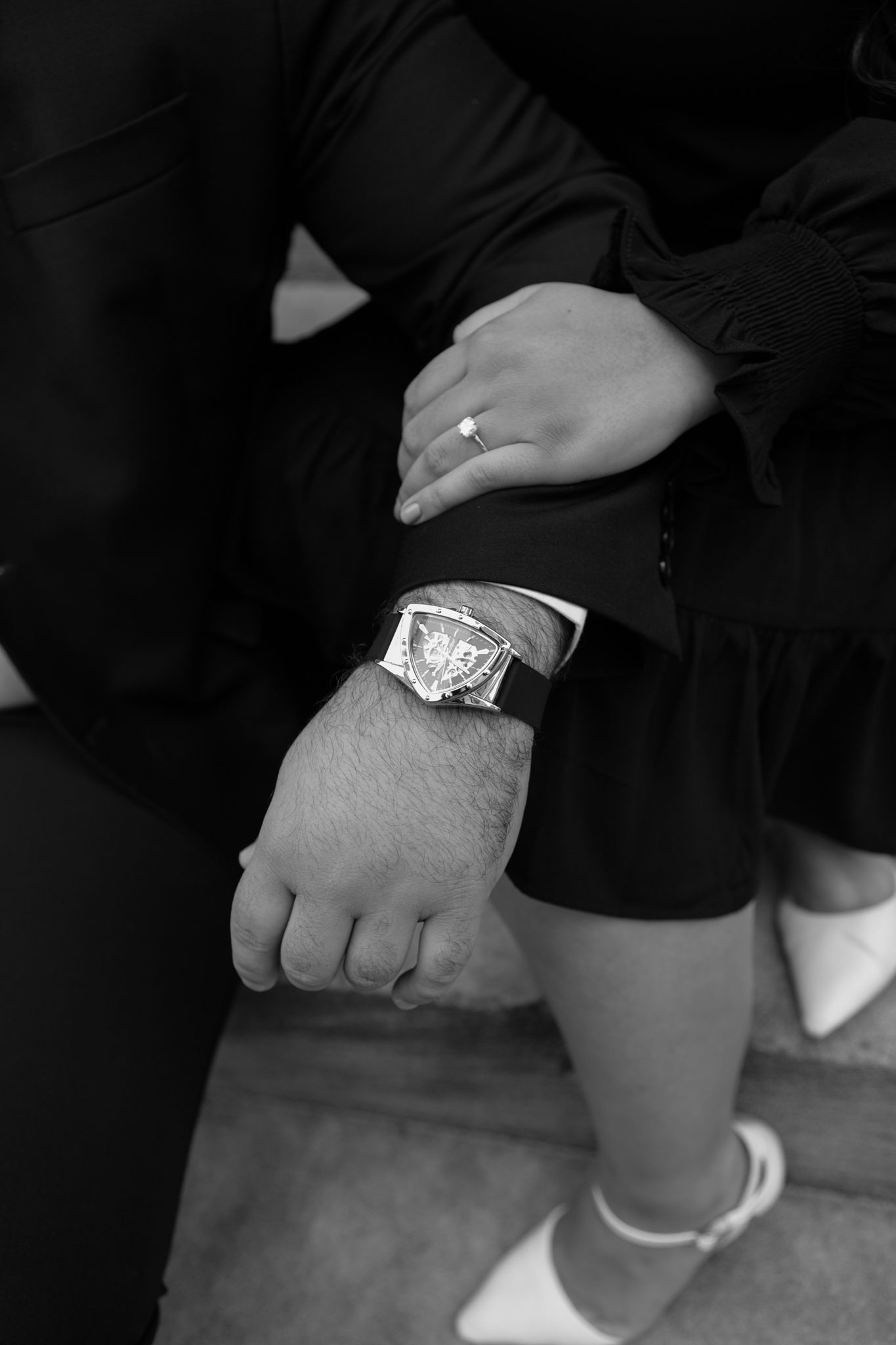 Elegant engaged couple smiling and embracing in downtown Louisville, with the woman showing her engagement ring