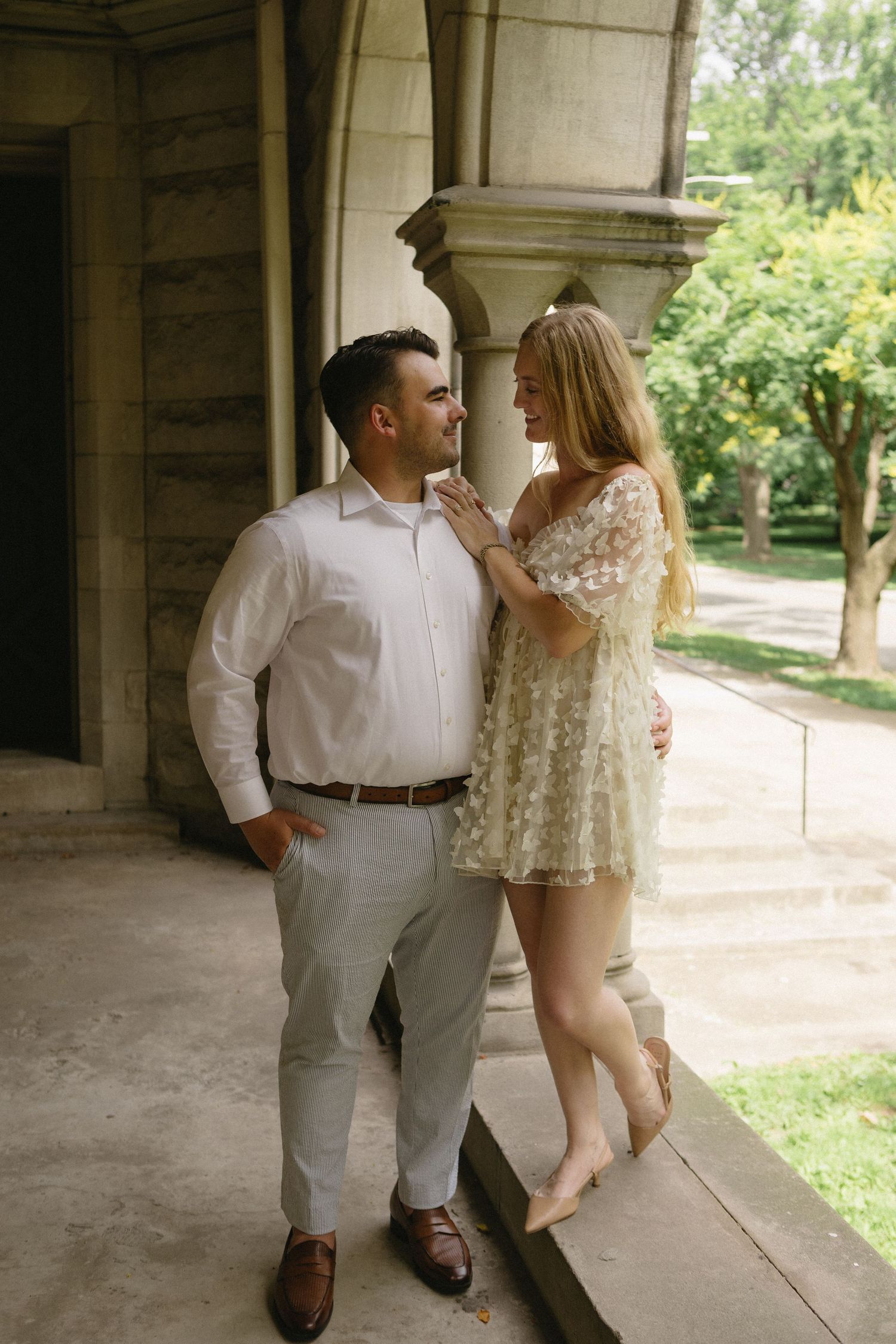 Romantic couple sharing an intimate moment under stone archway surrounded by greenery.