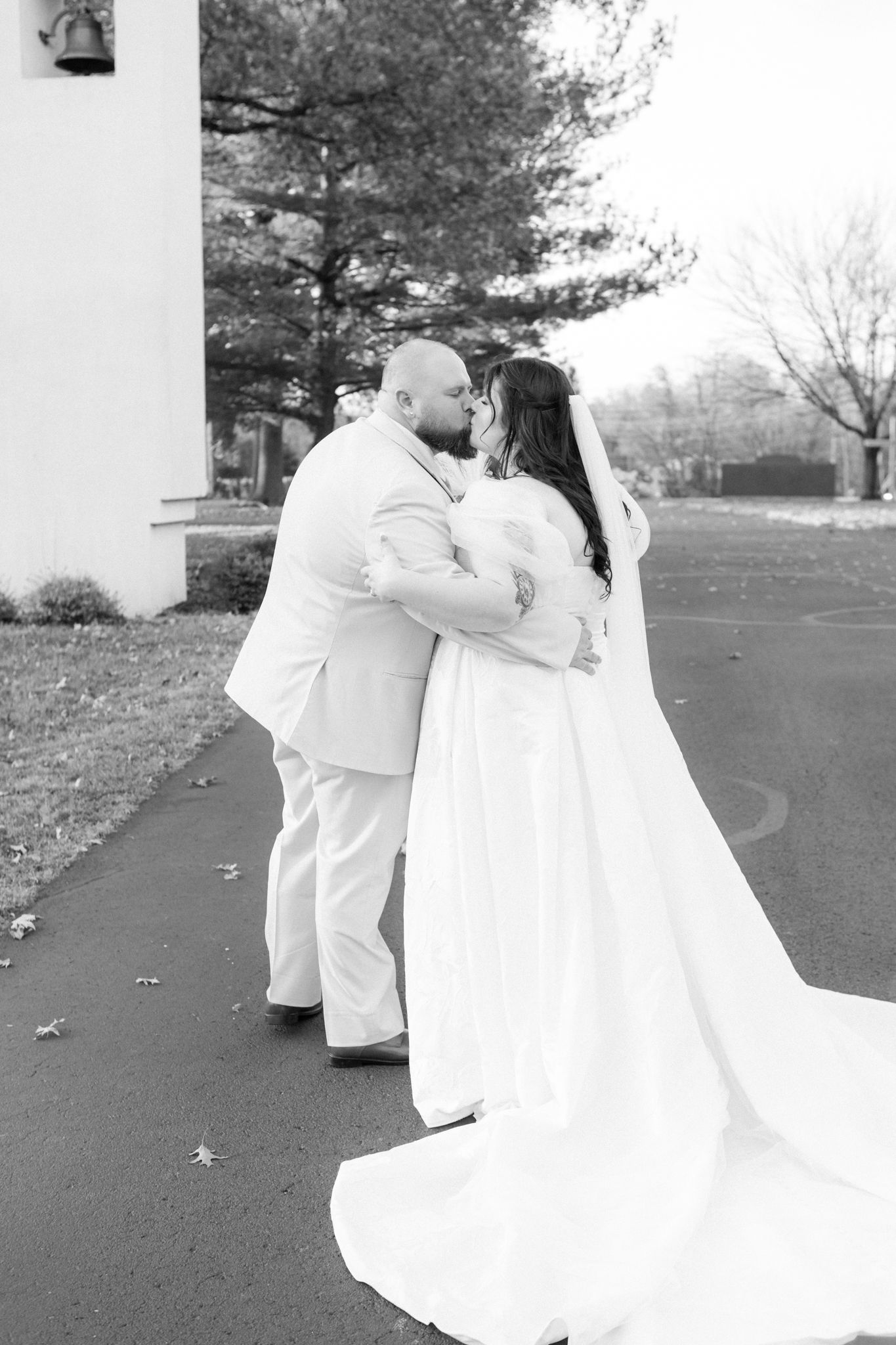 A romantic black and white wedding photo showing a couple embracing outdoors in formal attire.