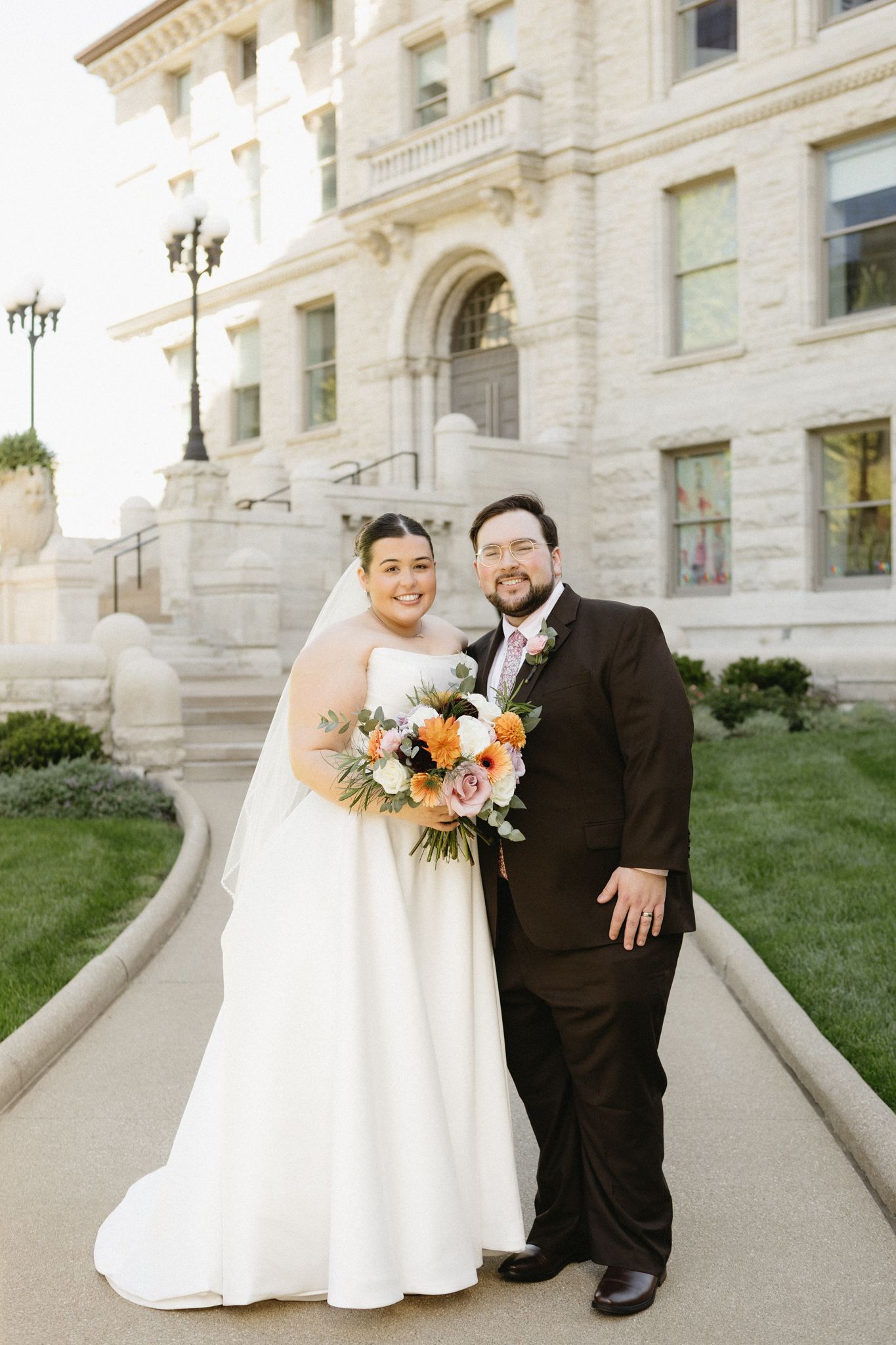 A bride and groom pose for portraits on white stone steps outside a grand government building.