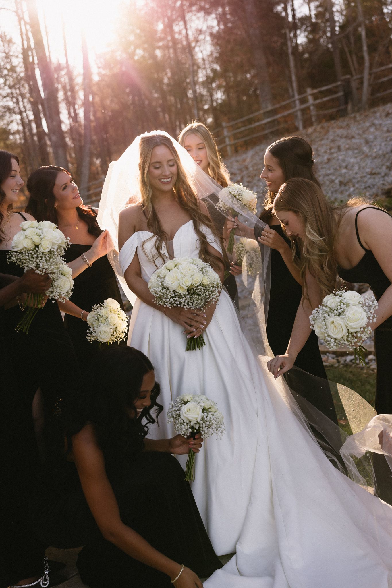 Bride and bridesmaids share candid laughing moment outdoors with white bouquets.