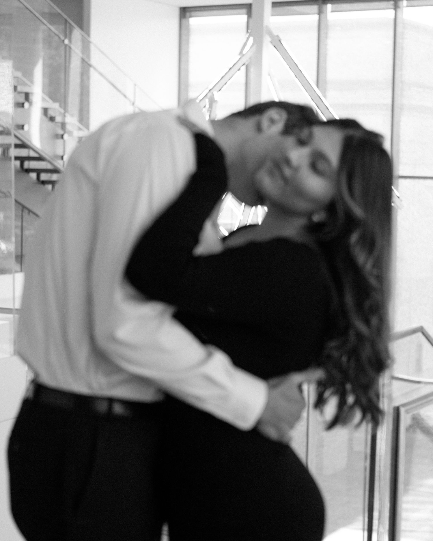 Elegant engaged couple smiling and embracing in downtown Louisville, with the woman showing her engagement ring