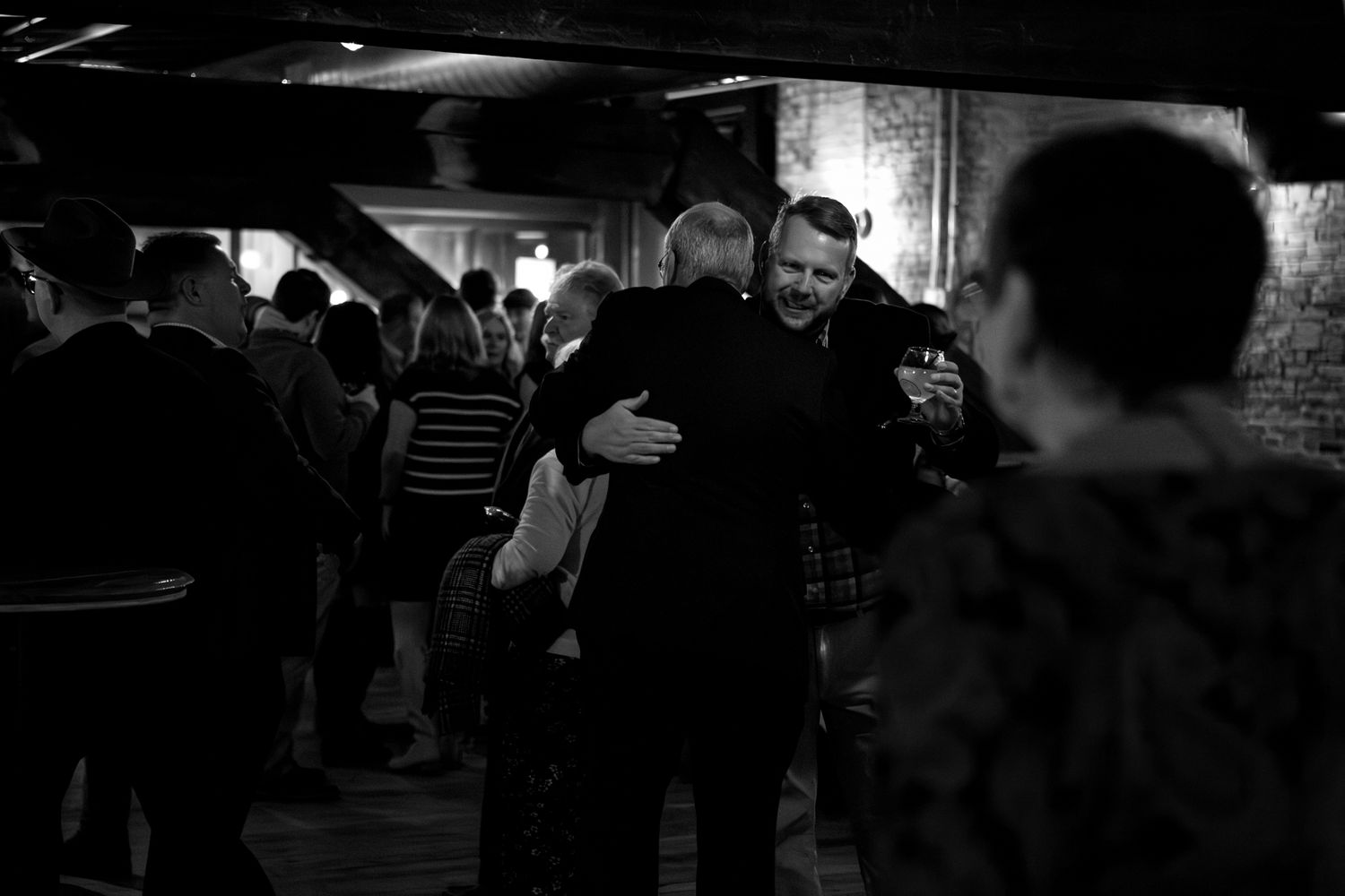Black and white photograph of guests mingling at a dimly lit indoor social gathering.